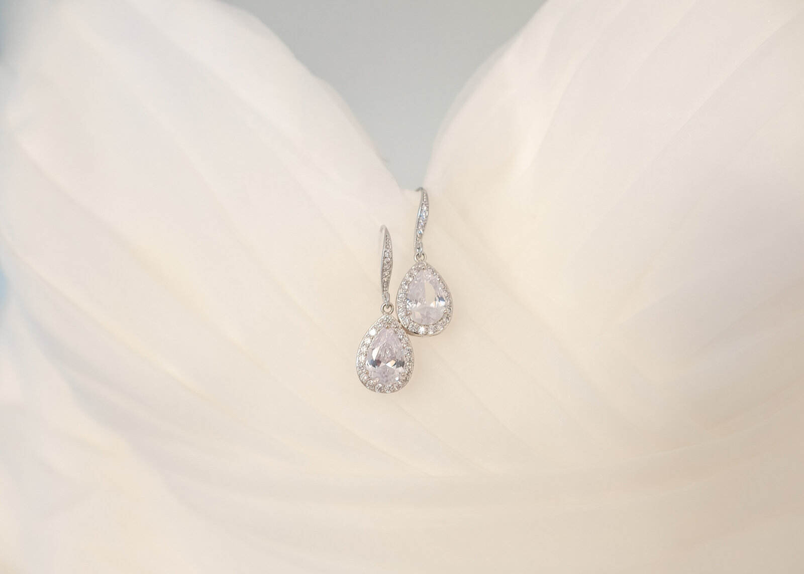 Close-up of sparkling teardrop bridal earrings resting on the soft, flowing fabric of a wedding dress, captured at a Wilmington, NC wedding, showcasing timeless elegance and refined bridal details.