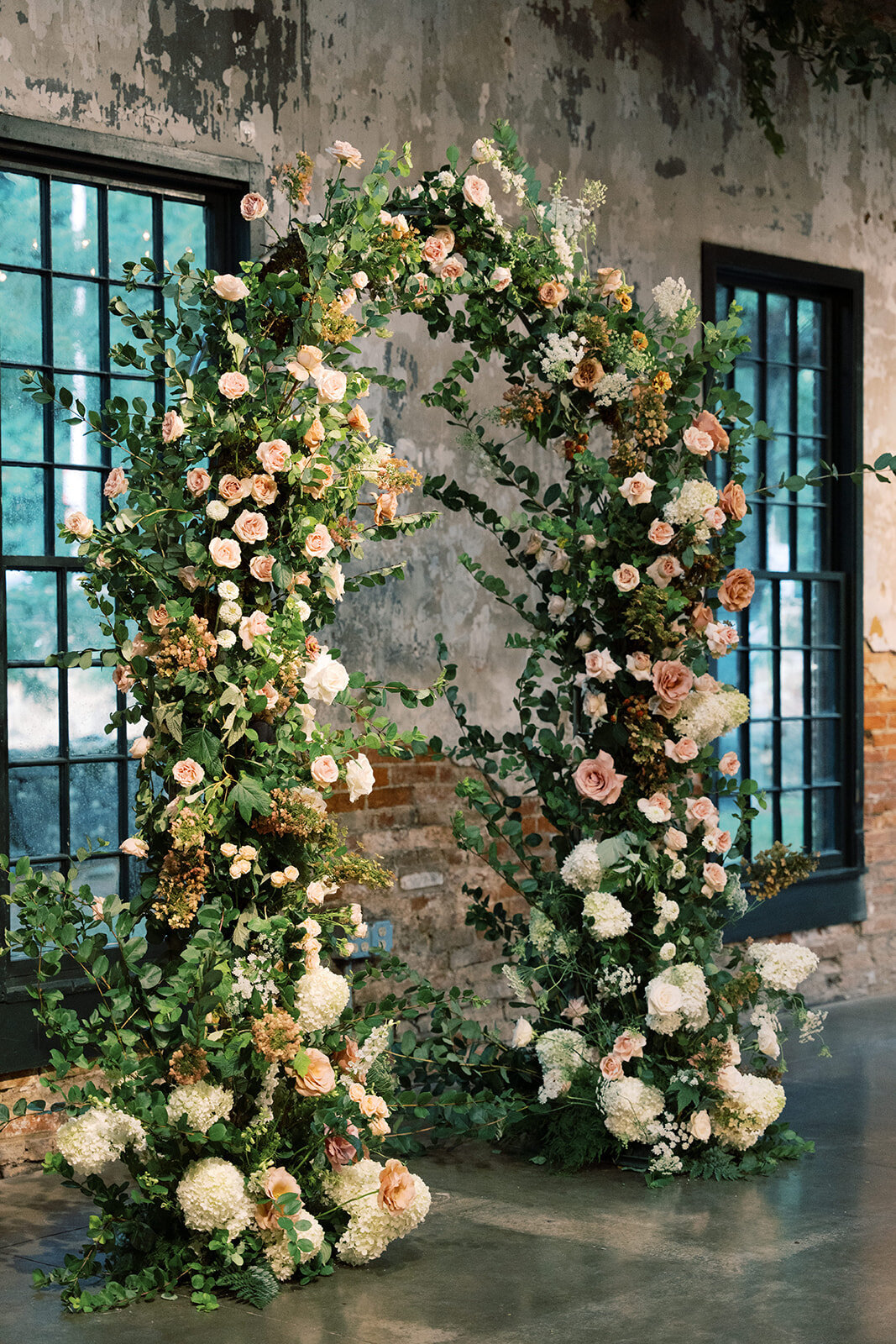 Full floral arch including white, blush, and peach garden roses, hydrangea, and lush vining greenery.