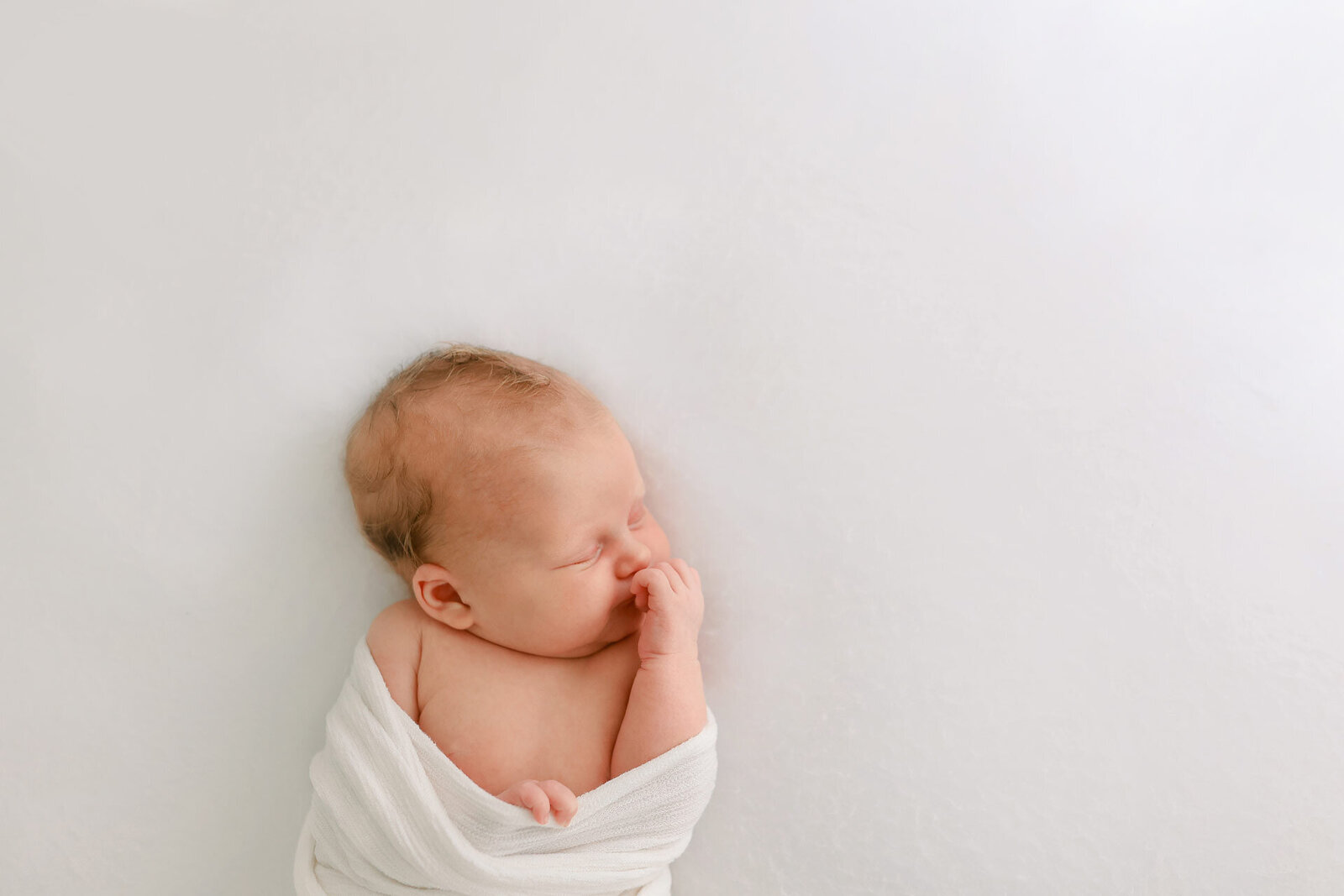 Neugeborenes beim Schlafen in einem weißen Deckchen bei einem Neugeborenenfotoshooting nahe Bielefeld.