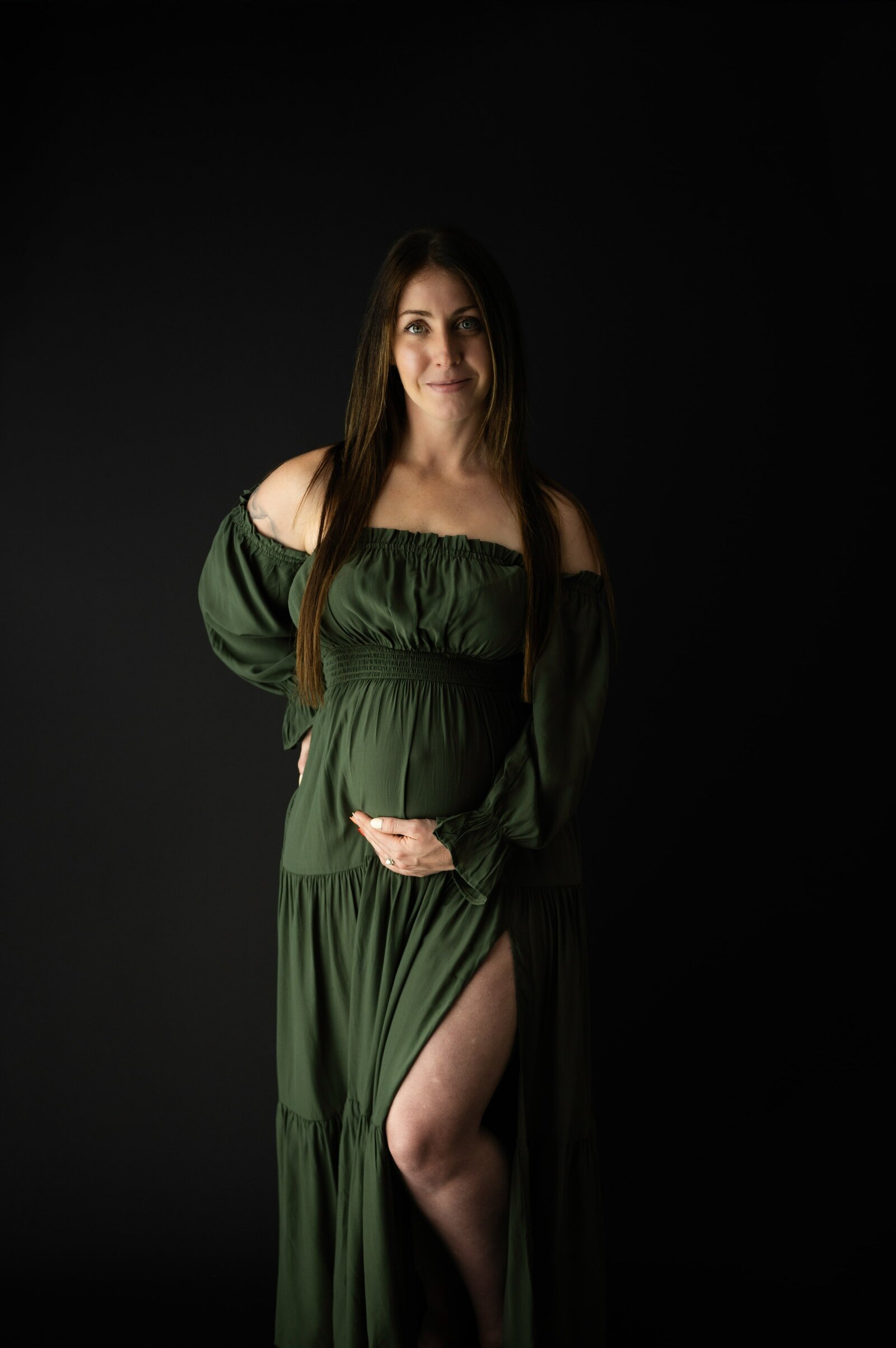 pregnant woman holding her stomach with on leg showing through green dress