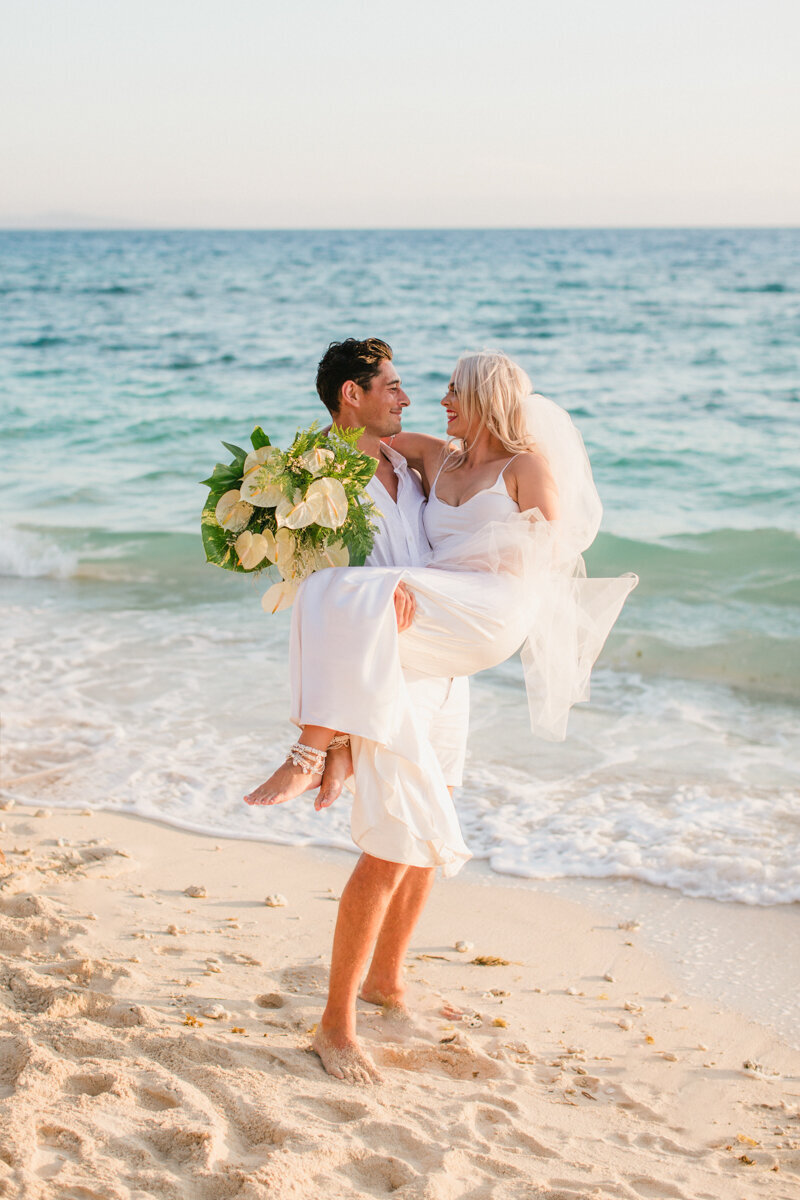 groom carrying bride and looking at her on the beach