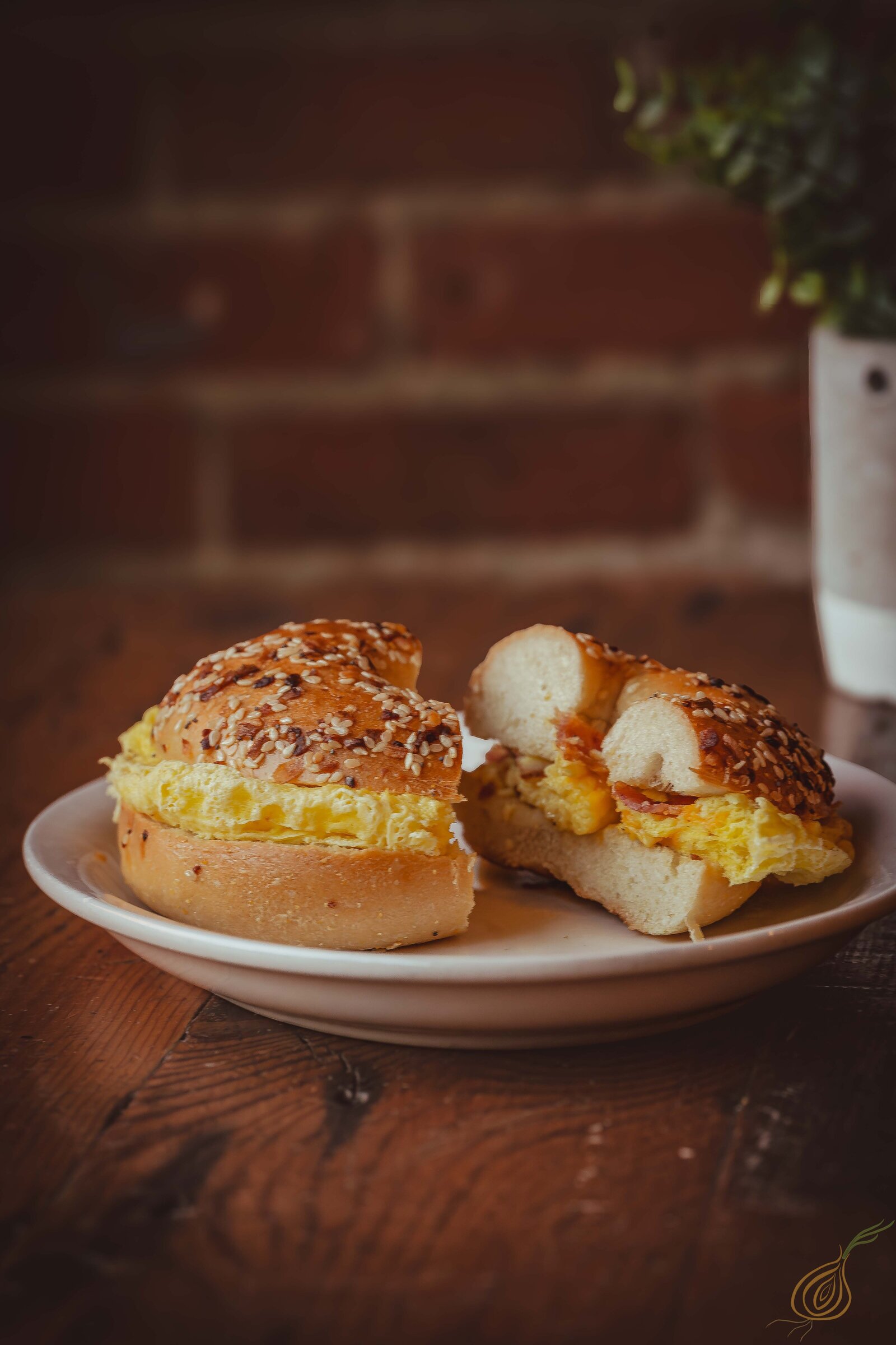 A delicious breakfast sandwich displayed on a plate, with a textured brick wall providing a warm background.