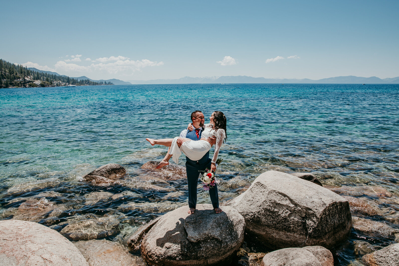 Groom lifting bride on the rocks by Lake Tahoe’s turquoise shoreline during their elopement.