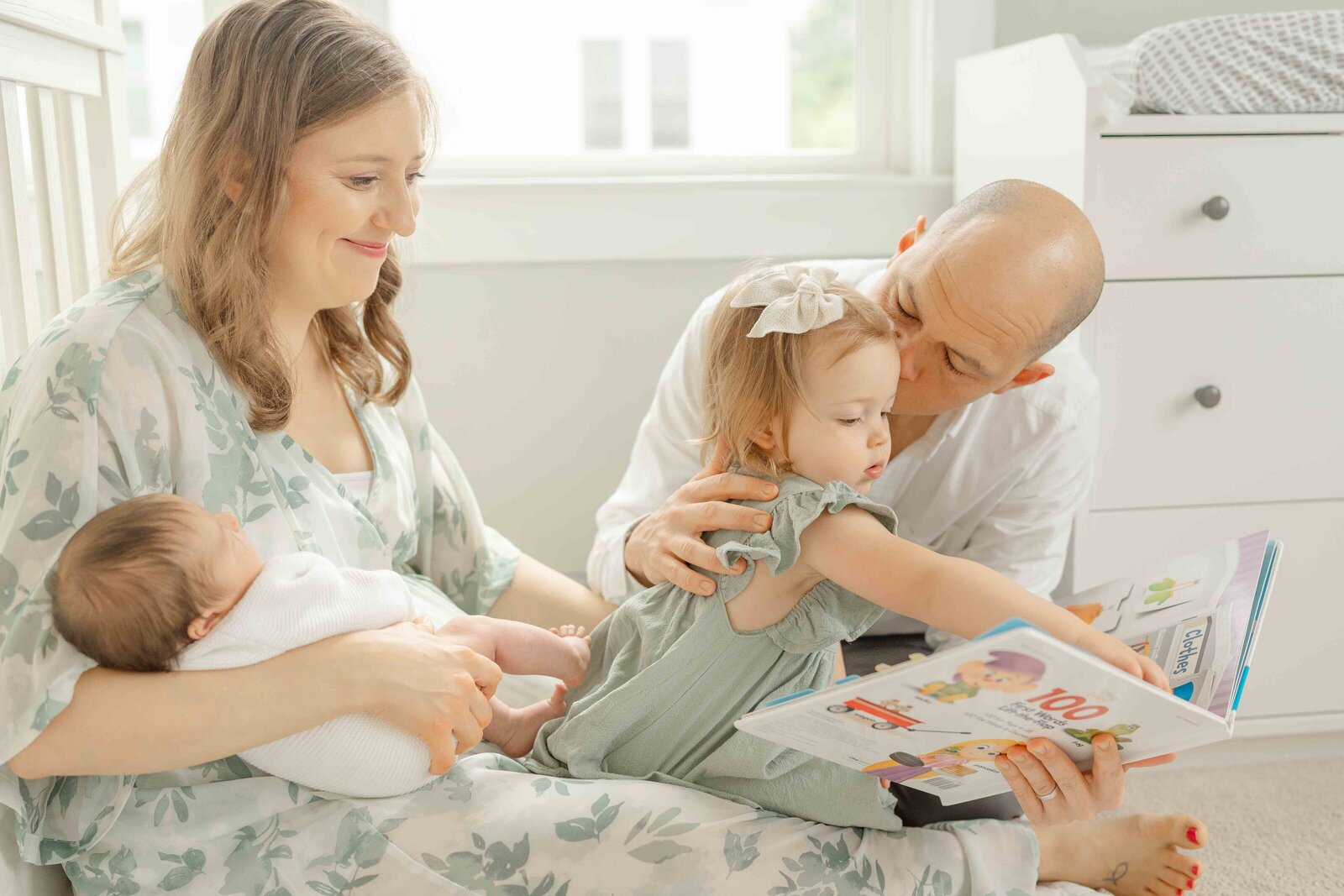dad kissing big sister while she reads a book during newborn session in Centreville, Virginia