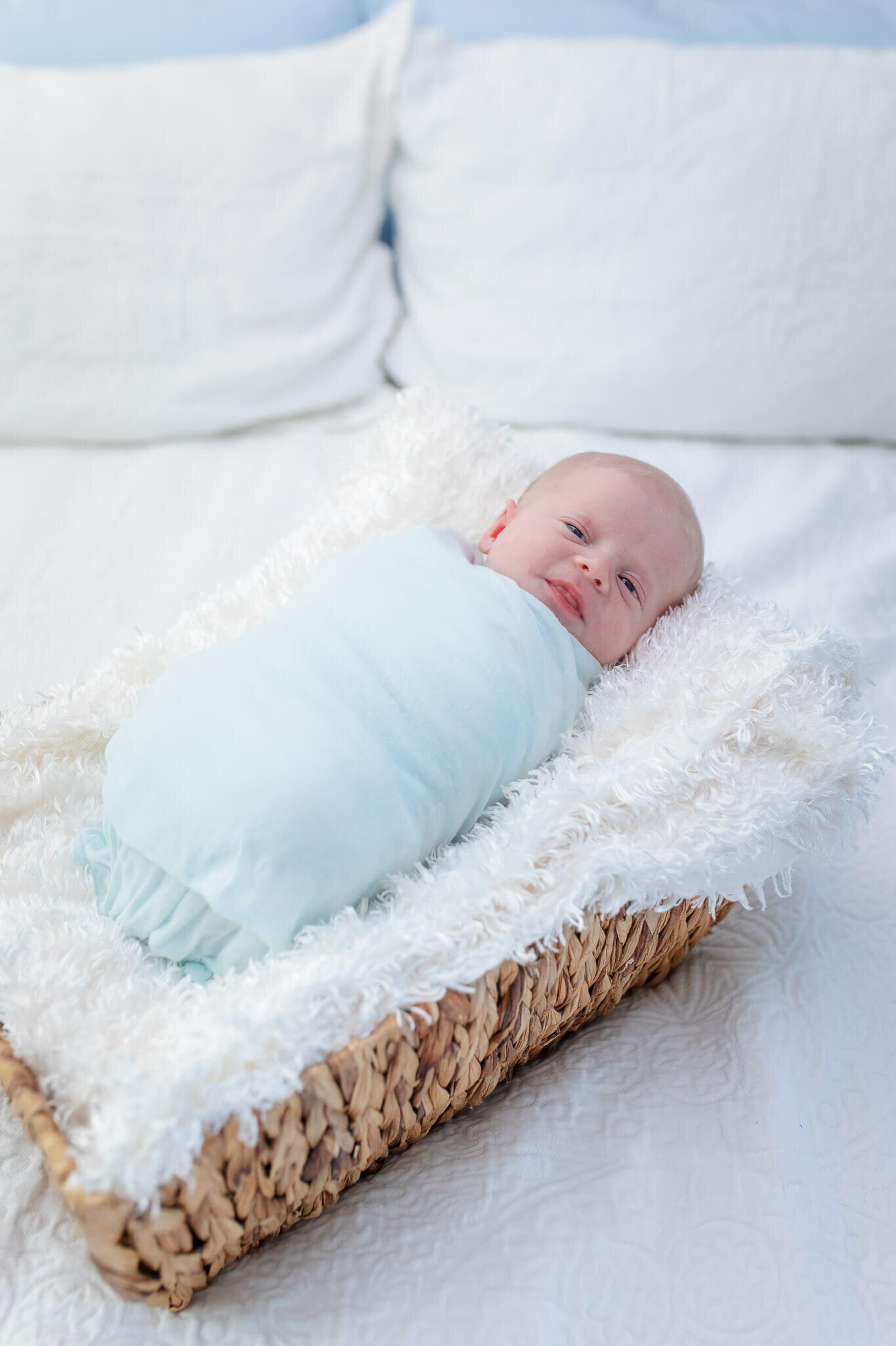 A newborn boy wrapped in blue laying on a white blanket in a basket.