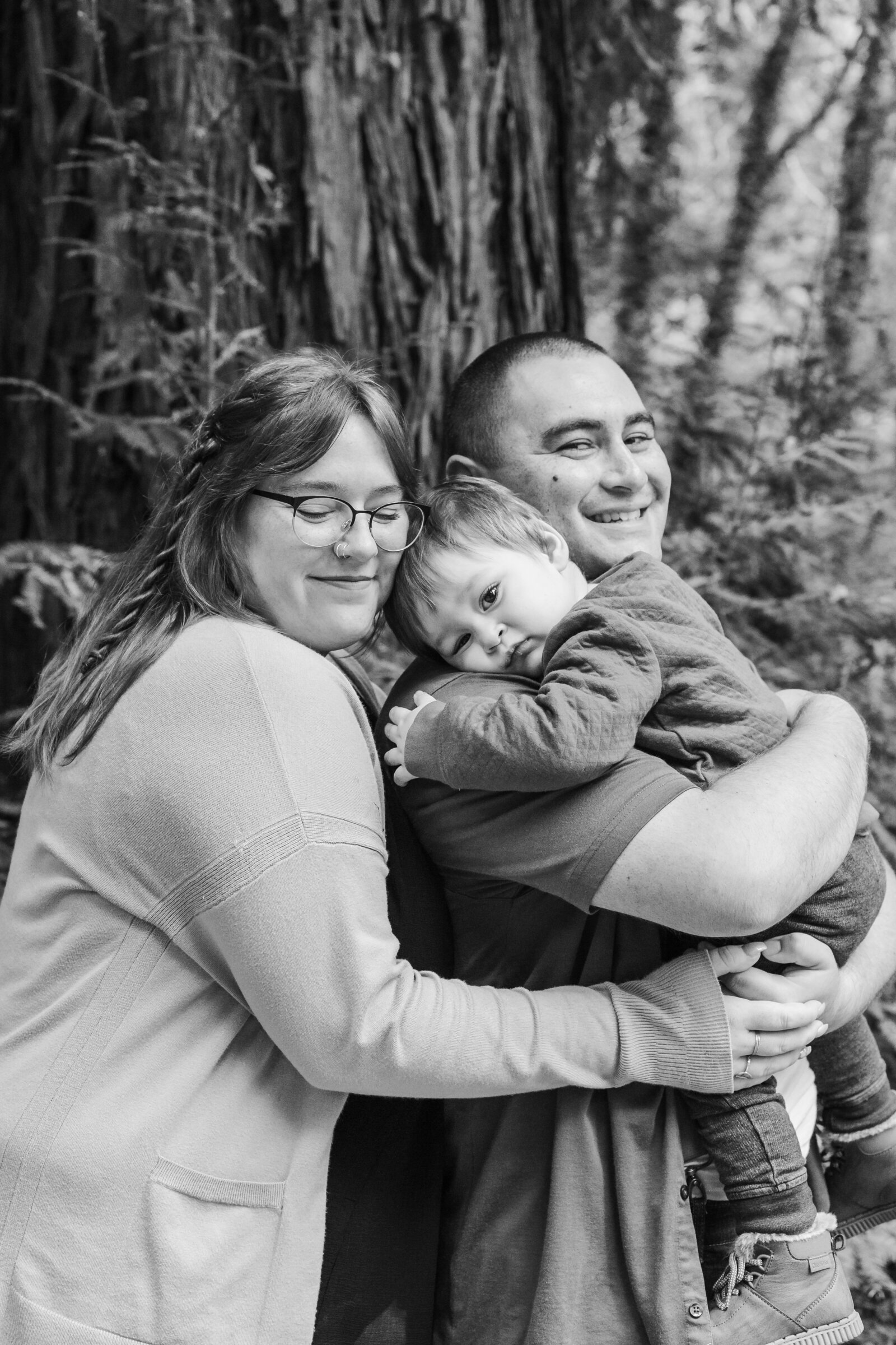 A family of 3 poses for photos in a forest in Santa Cruz, Ca.