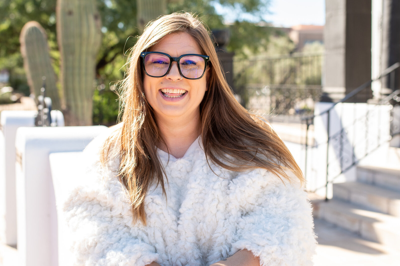 Smiling woman with long hair and glasses wearing a textured white sweater outdoors, photographed by Vyrl Photo, highlighting Tucson brand photography.