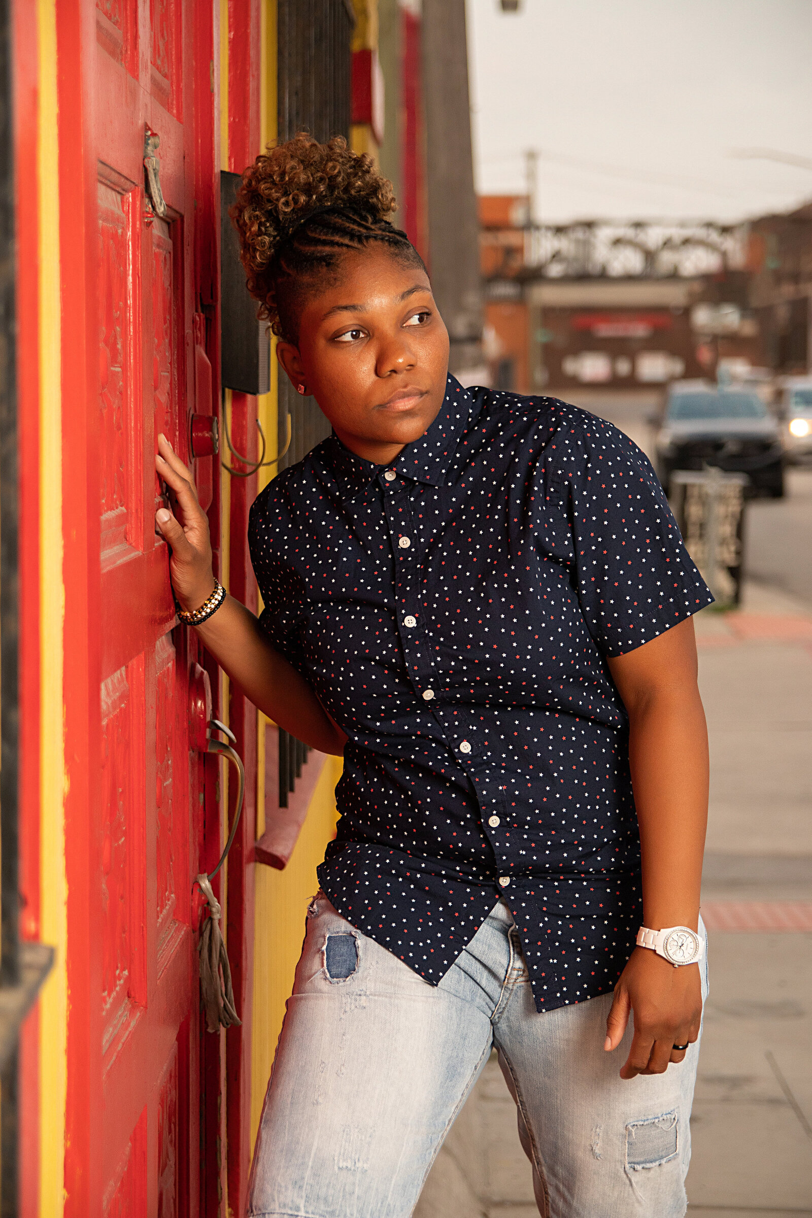Woman with navy blue printed top and blue jeans leaning against a door