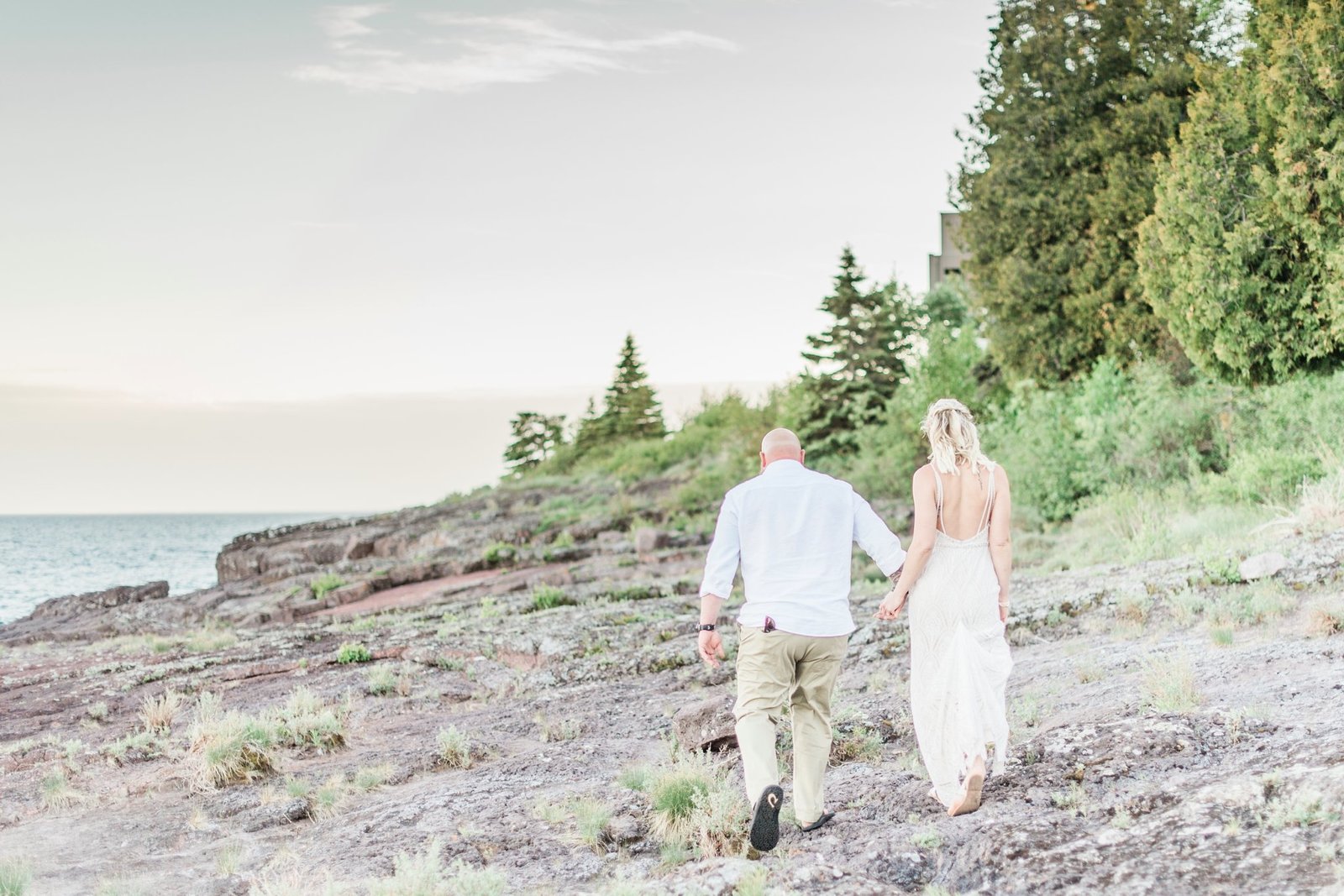 A couple walk away from the camera along the rocks on Lake Superior after their Minnesota wedding.