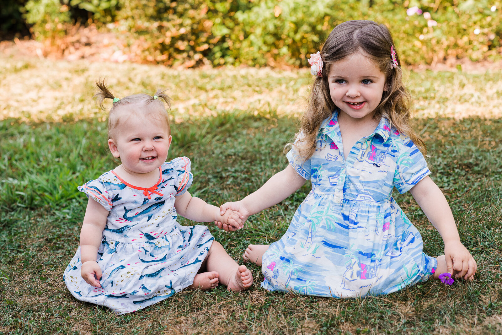 sisters hold hand sitting in grass