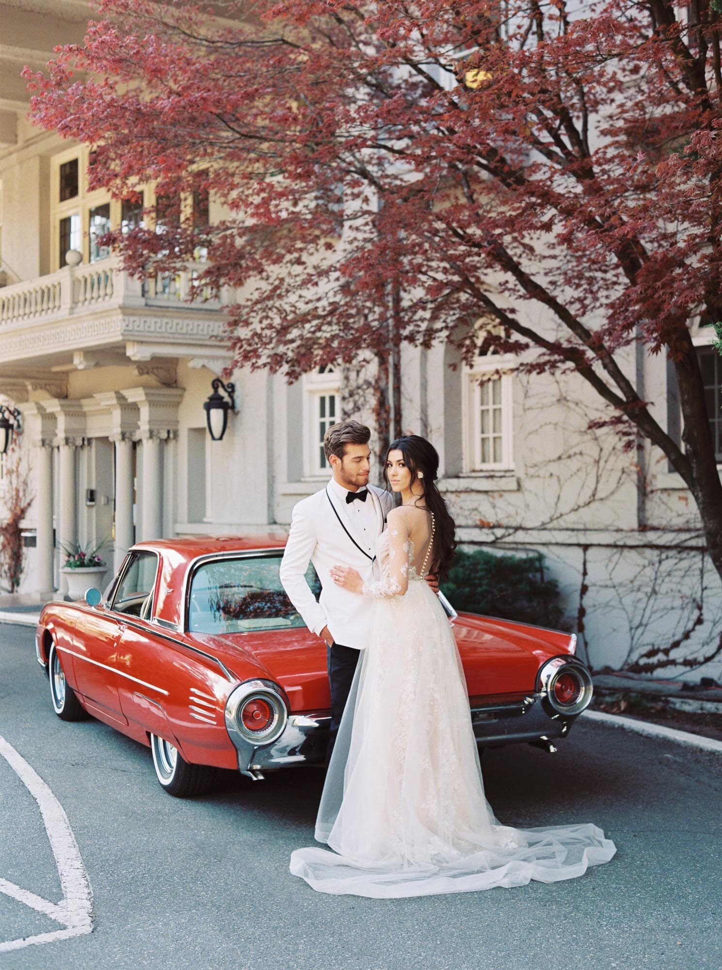 Bride and groom posing with their classic red car