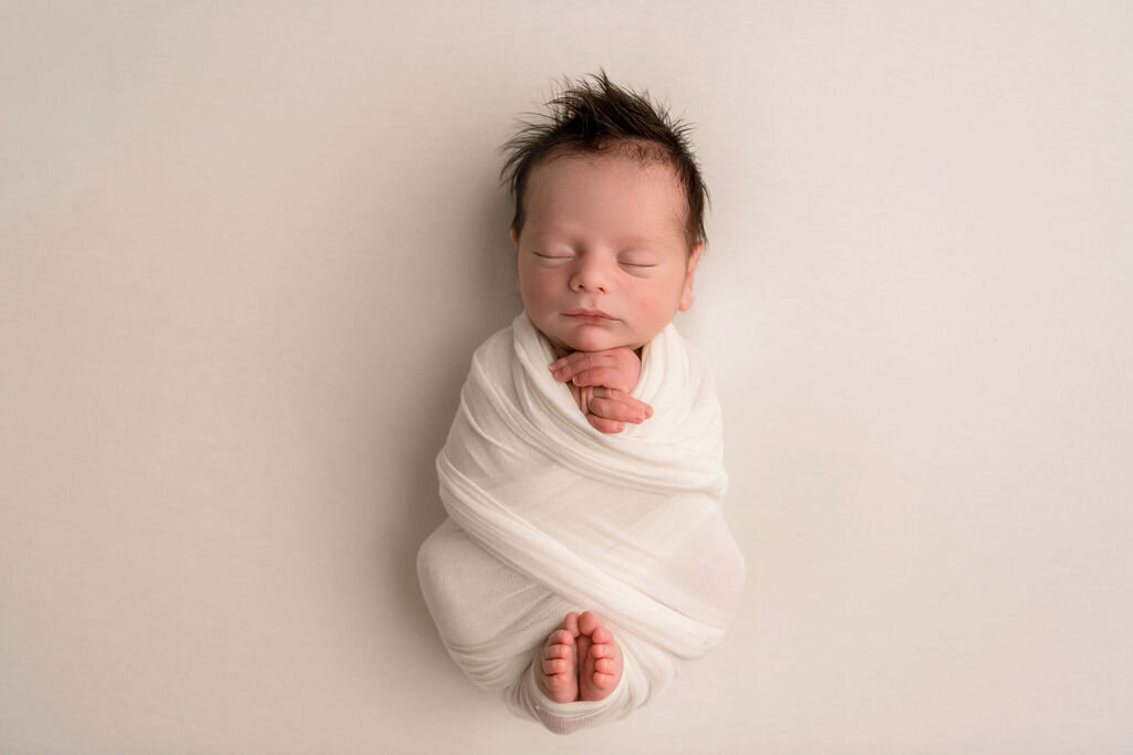 Peaceful sleeping newborn baby swaddled in cream white wrap against neutral backdrop