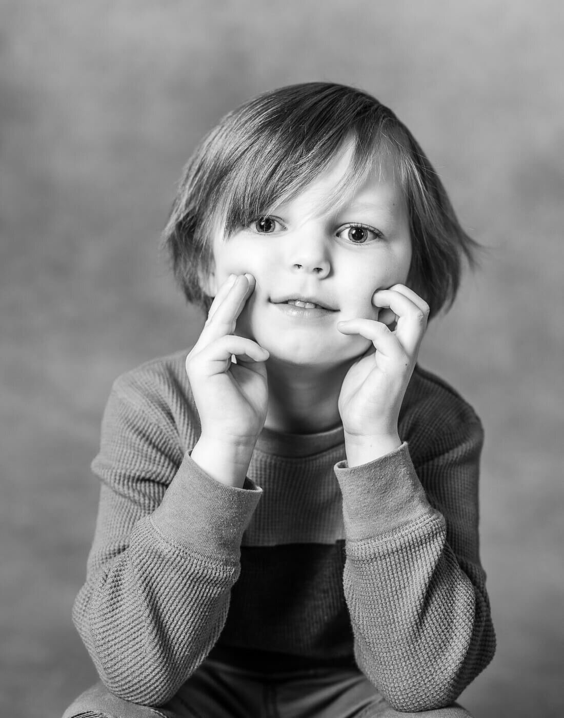 A child smiles with their hands on their cheeks.