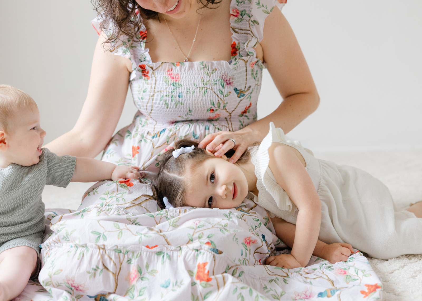 little girl laying in mom's lap looks at the camera while baby brother reaches for her