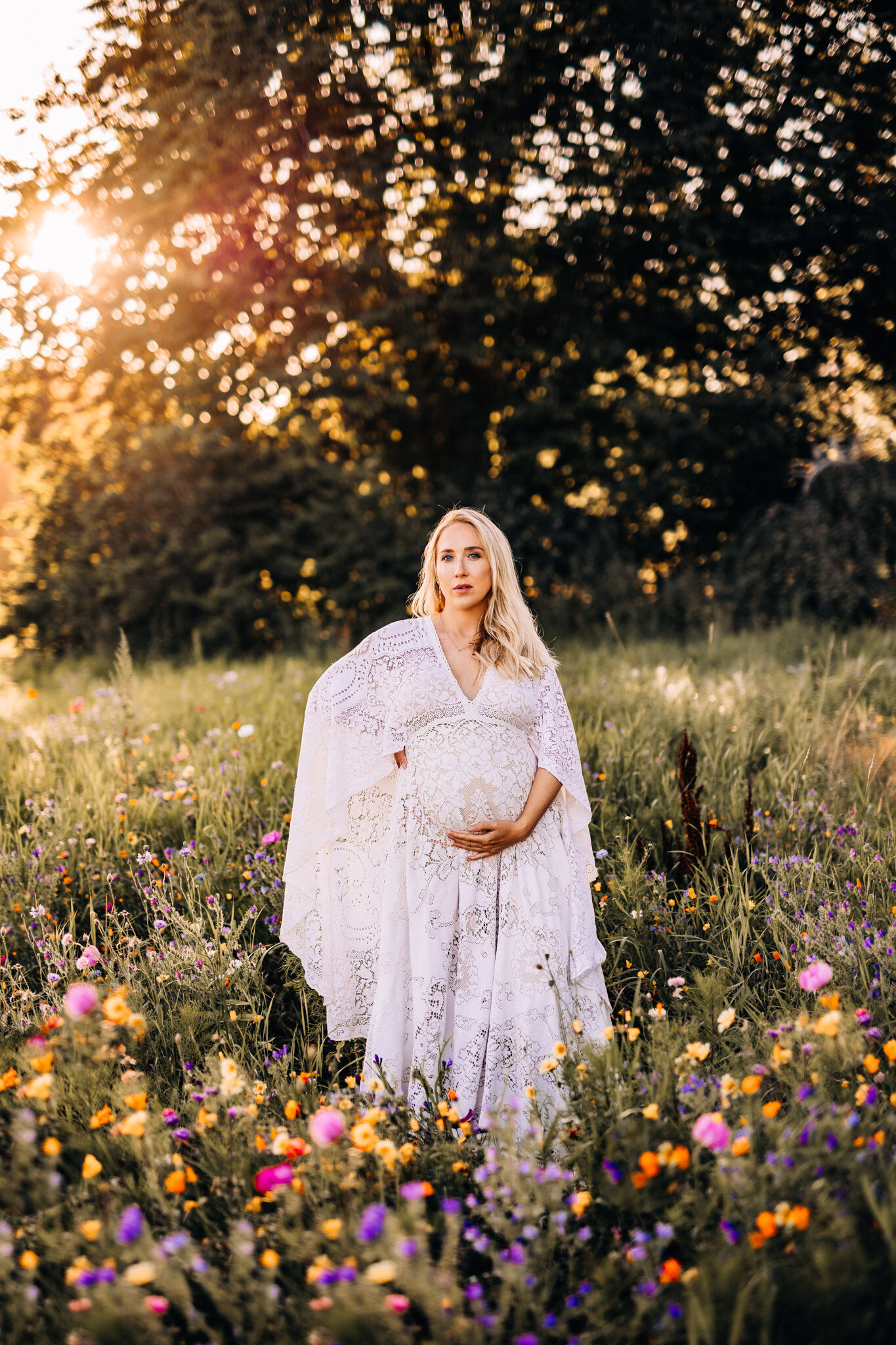 en gravid kvinna står på ett blomfält iklädd en bohemisk gravidklänning