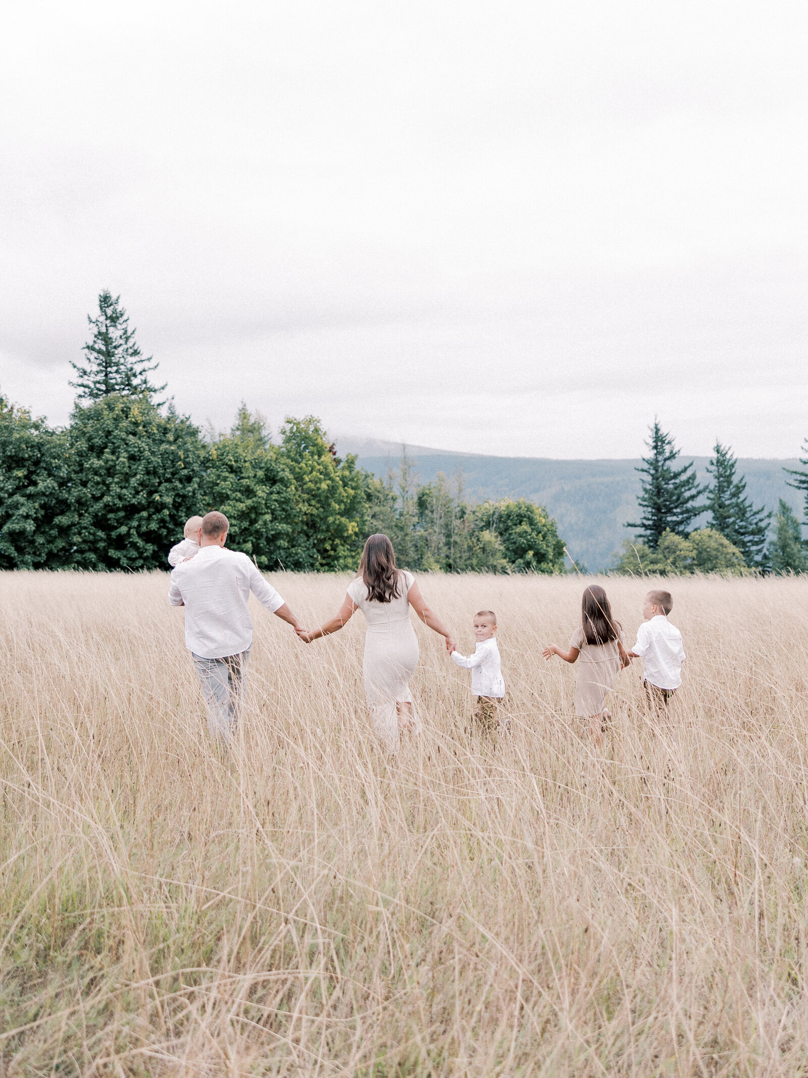 Family with four children holding hands walking through a field