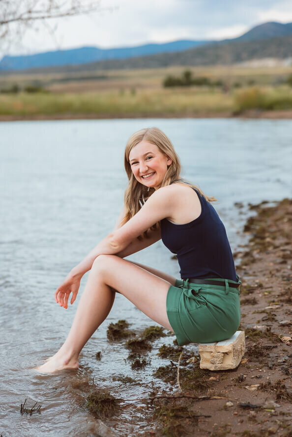 Girl sits on a rock and smiles at camera at Chatfield Lake.