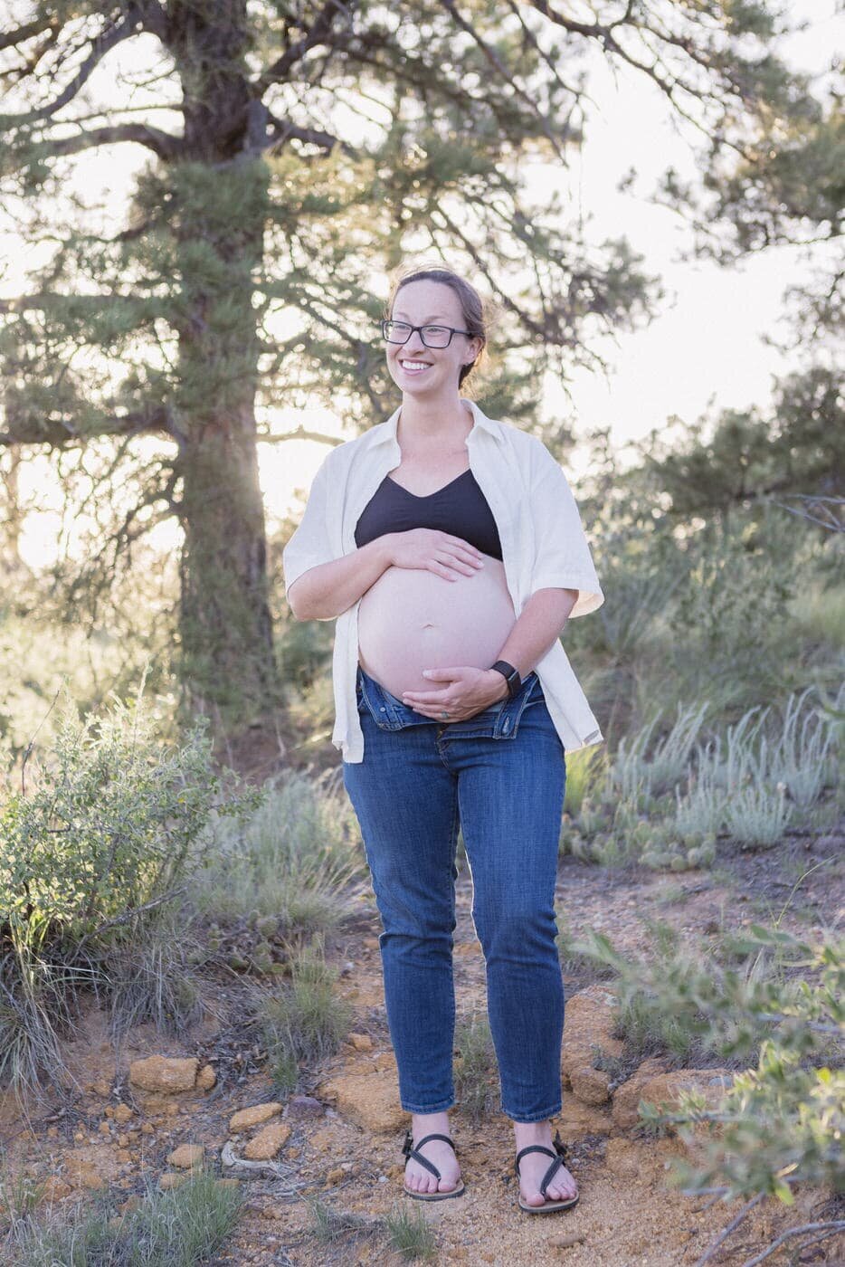 A pregnant woman poses for her maternity portrait by holding her belly and looking up and smiling. 