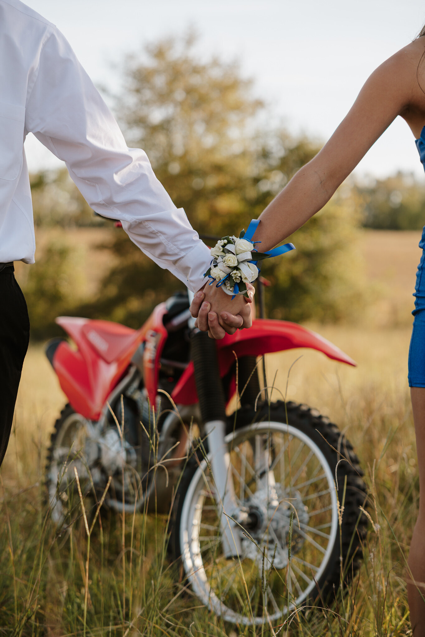 Outdoor homecoming couples photoshoot in Aiken SC - teens holding hands in front of a red dirt bike, wearing their HOCO outfits.