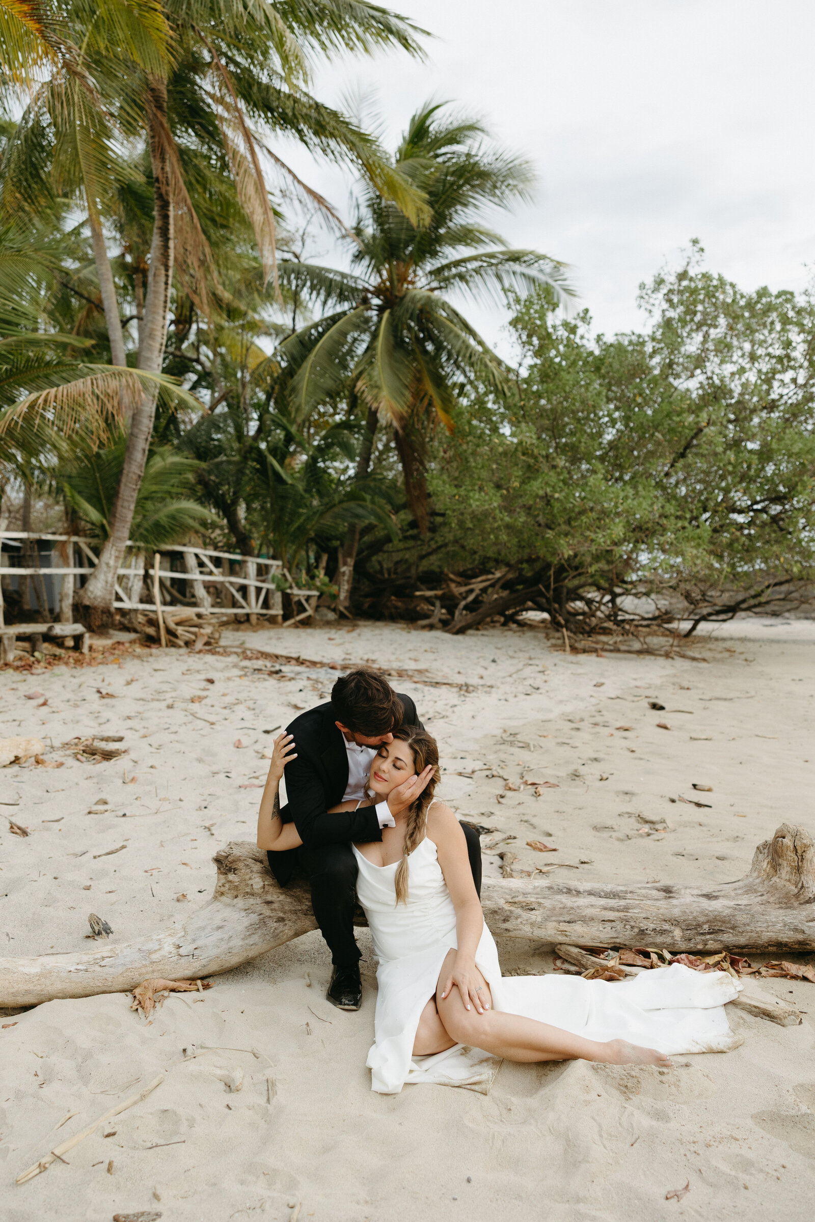 A bride and groom sit in the sand together after getting married on a Costa Rican beach.