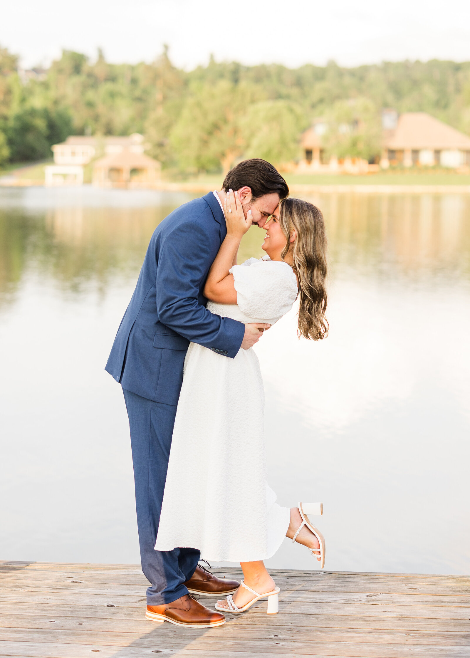 Julianna and Josh embracing on a dock with a serene lakeside backdrop, captured by Abby Bell Photography.