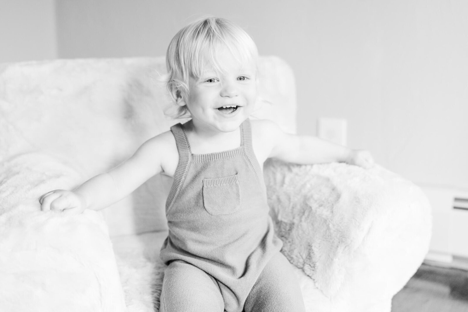 Toddler smiles from his chair, black and white