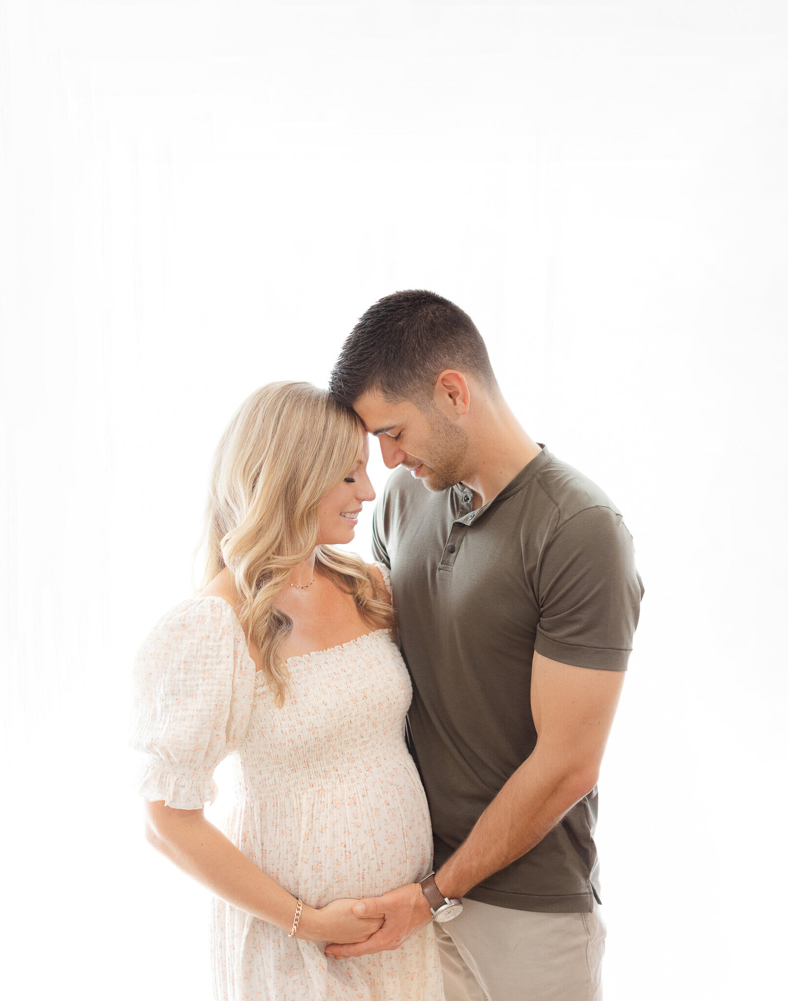 young couple holds baby bump with closed eyes smiling