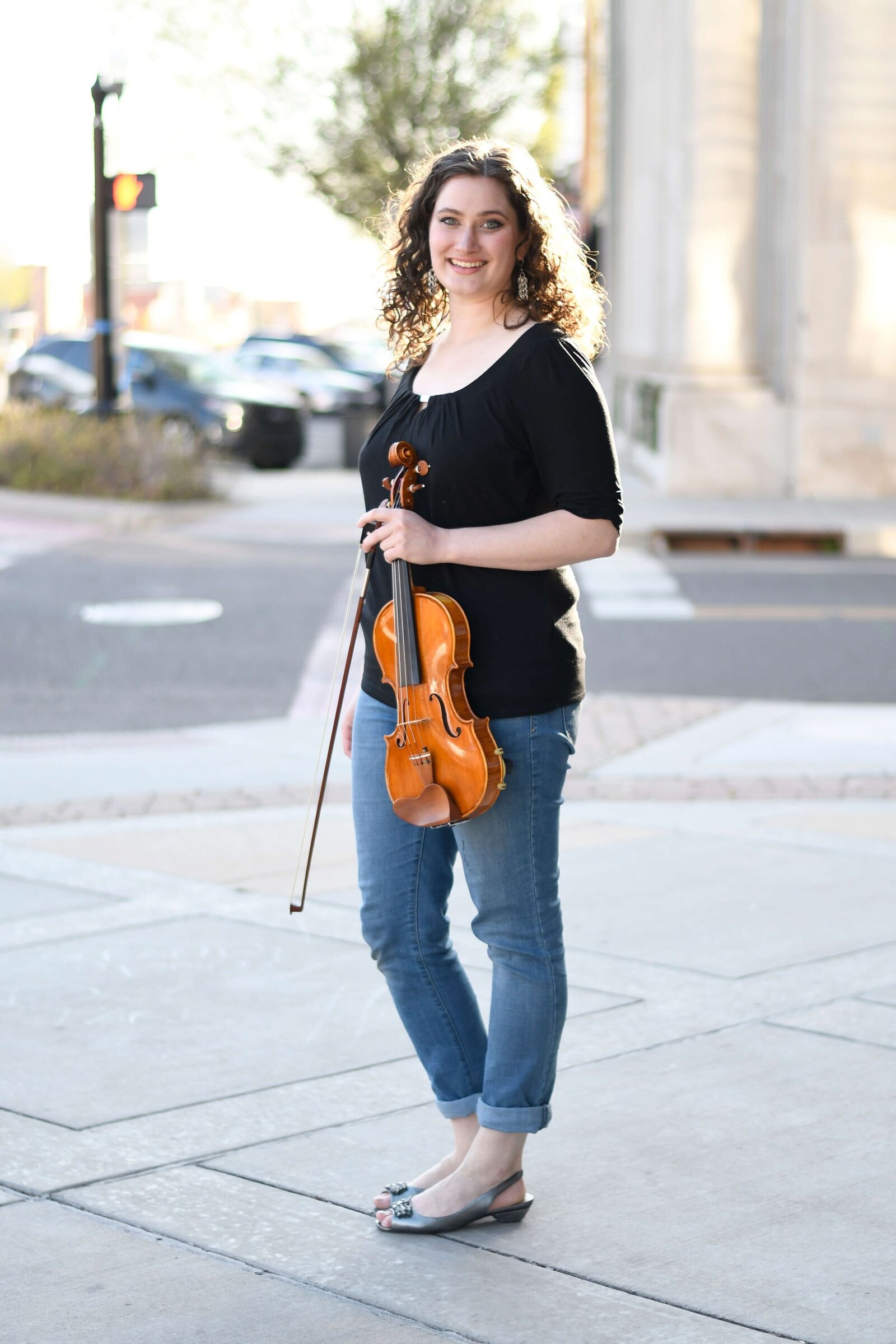 Violin teacher Erika Burns stands with her violin at a street corner.