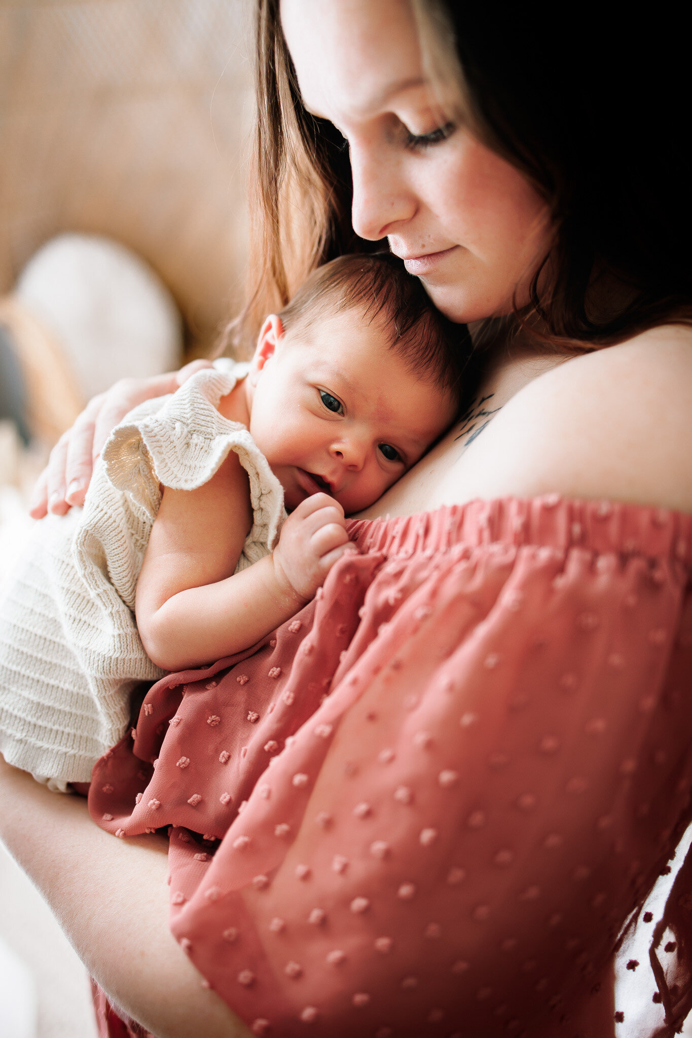 Newborn baby girl in a cream knit dress snuggles up on her mothers chest wearing a light pink dress