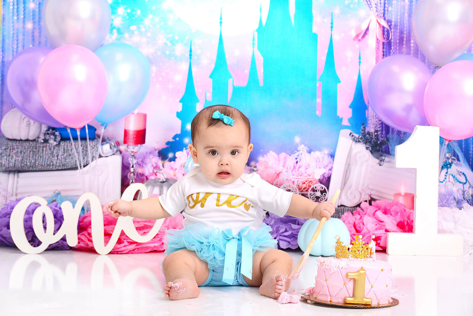 girl wearing a one romper and blue tutu at her cinderella themed cake smash shoot