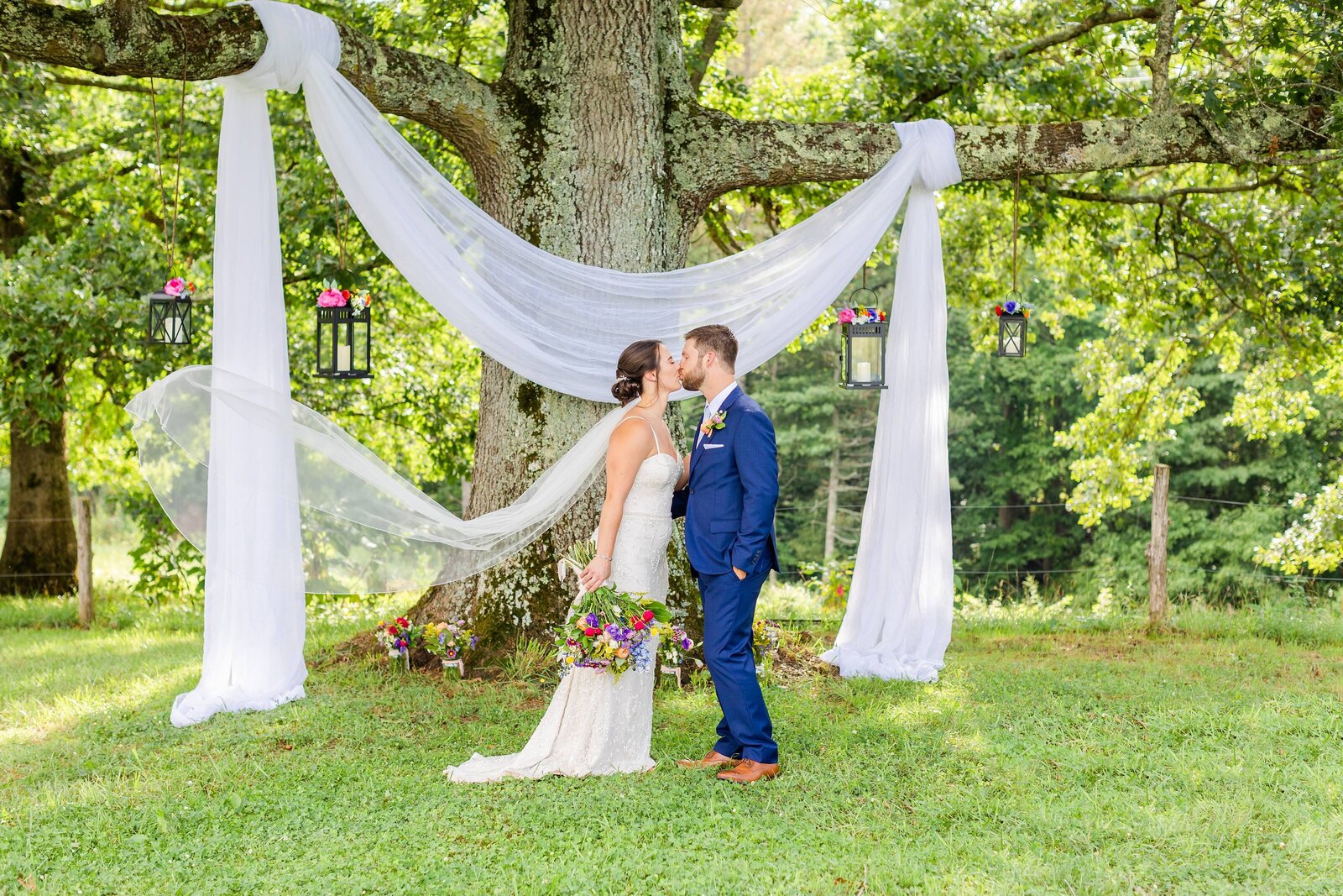 bride and groom kissing in front of big oak tree with veil in the wind