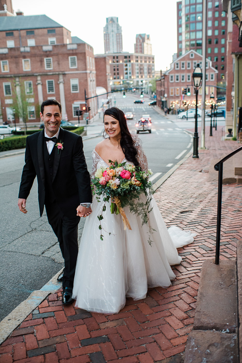 bride and groom walking with city in background