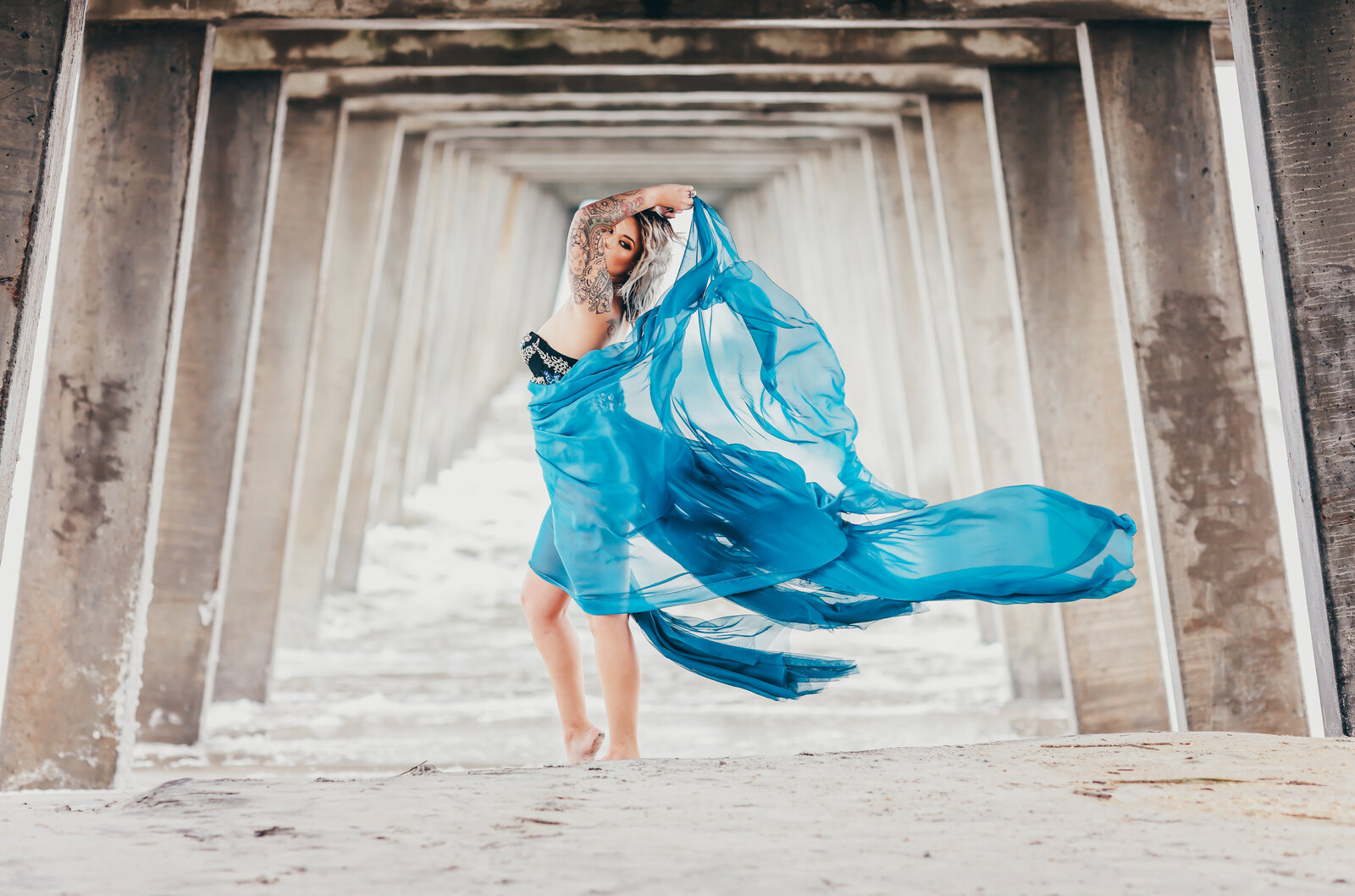 Woman in flowy blue gown under bridge looking sideways
