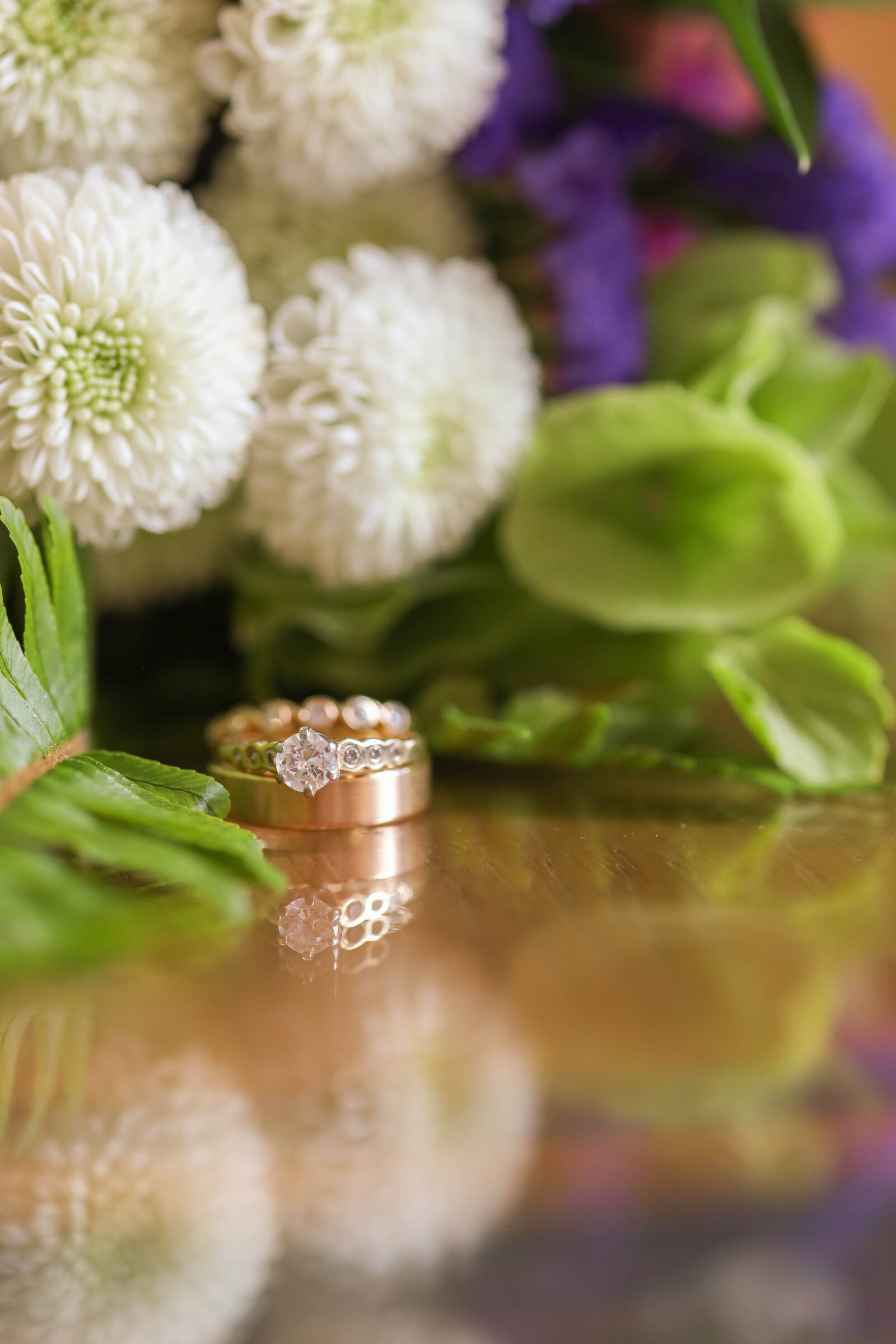 Wedding rings stacked, sitting next to the bridal bouquet, capturing a timeless and romantic detail shot.