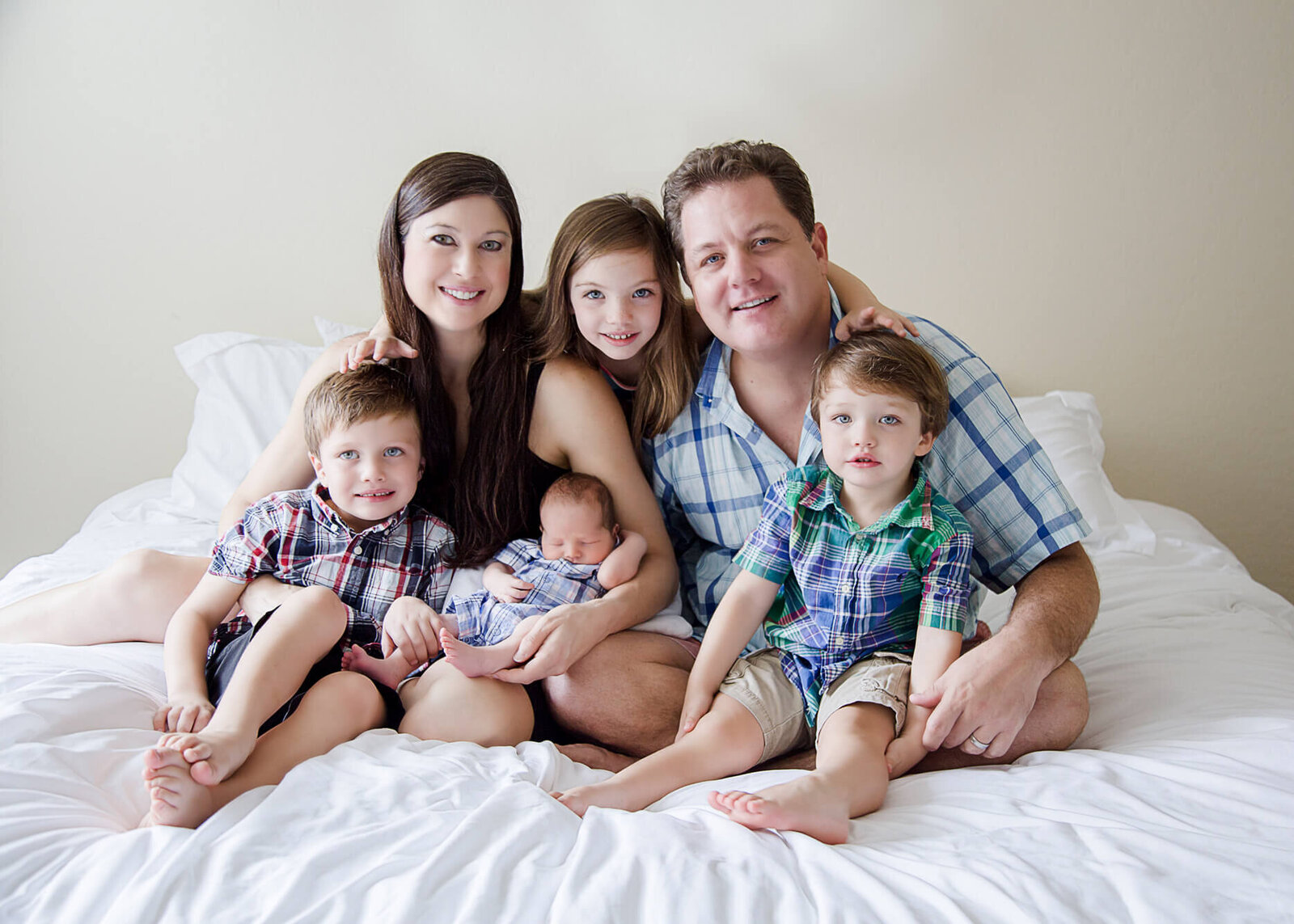 Family with 4 kids in plaid siting on white bed