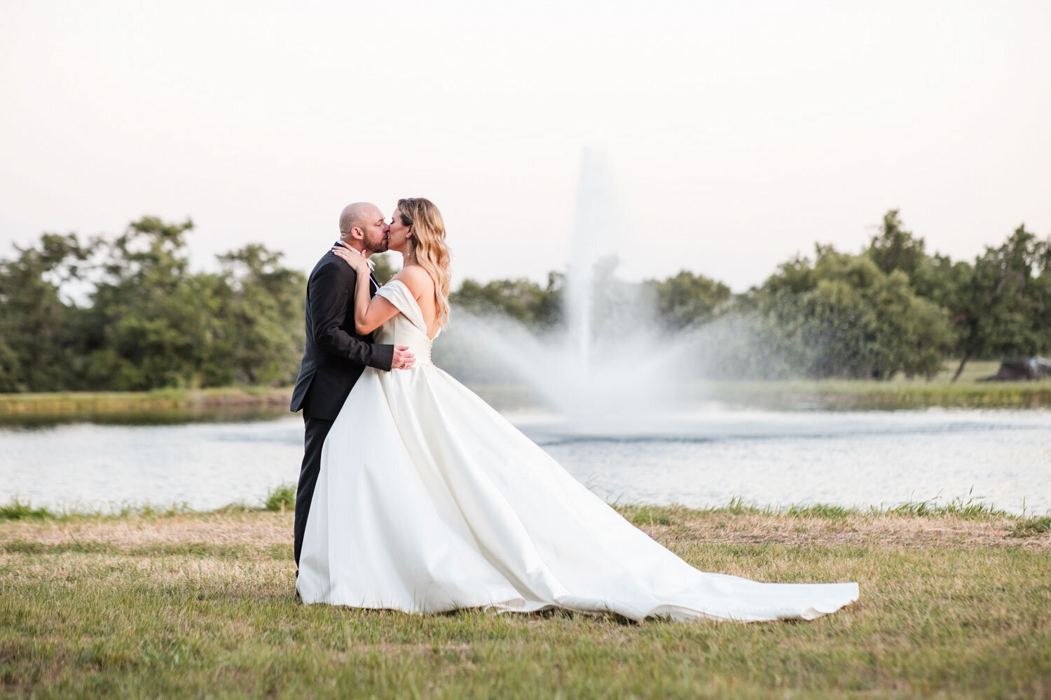 bride and groom kissing in front of pond with fountain