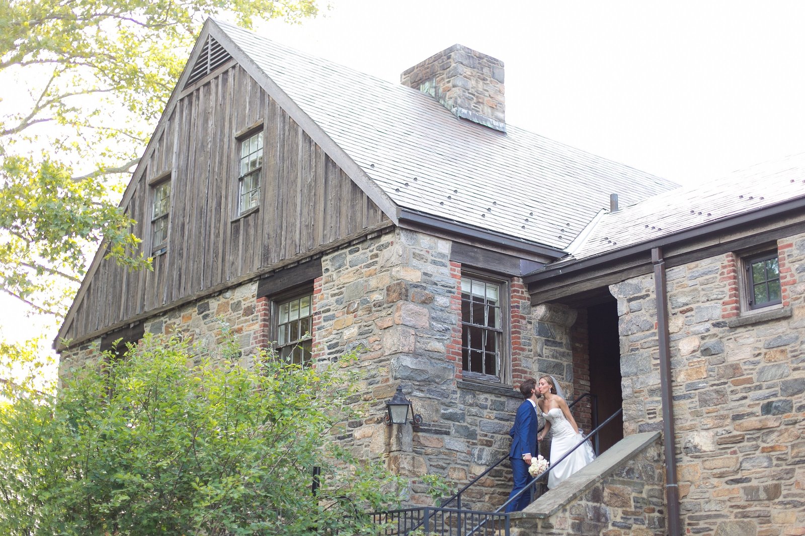 Bride and Groom kissing in front of stone barn from far away at Blue Hill Stone Barn wedding in Westchester, New York Photo
