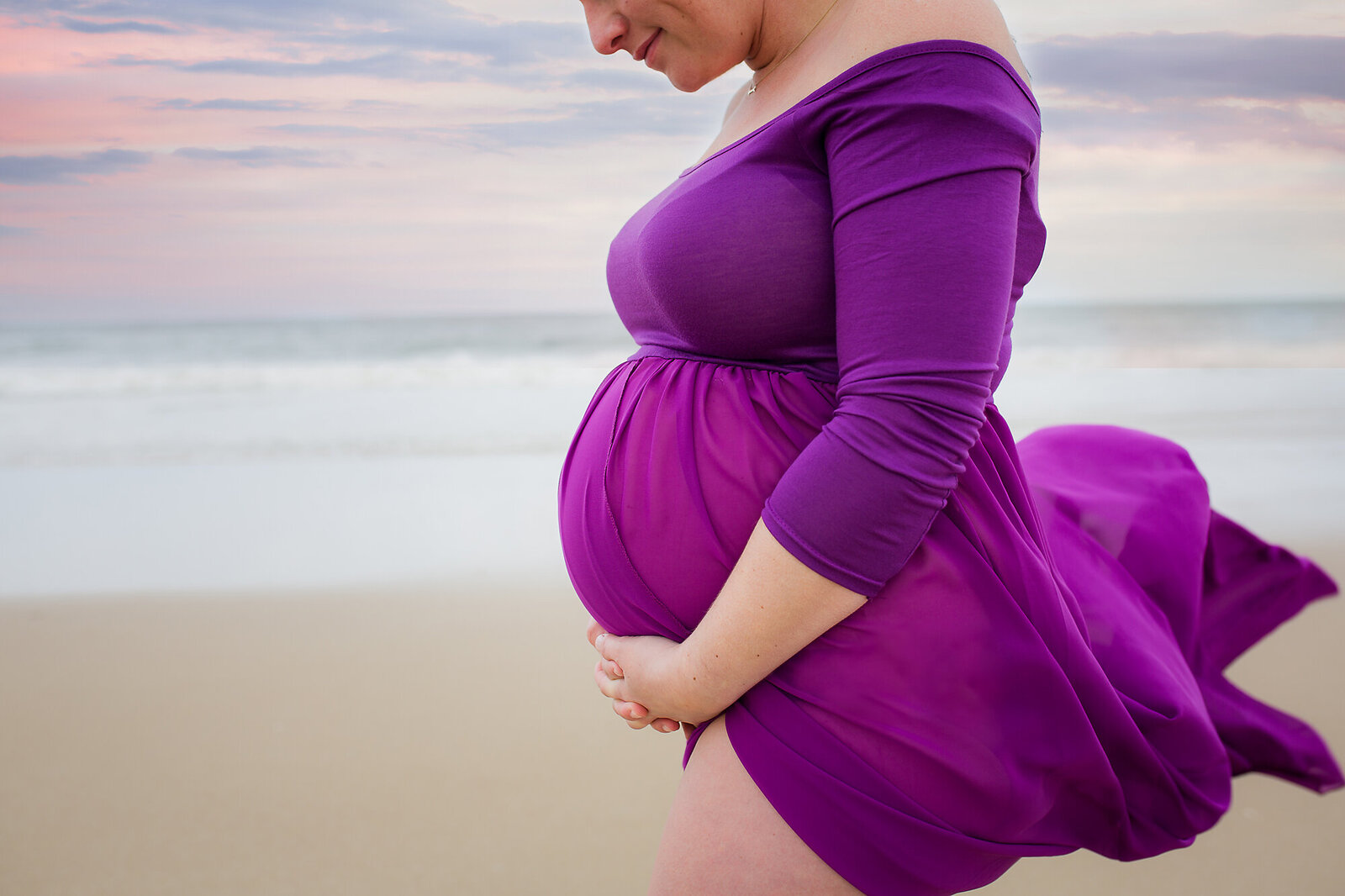 pregnant woman in purple dress blowing in the wind on the beac