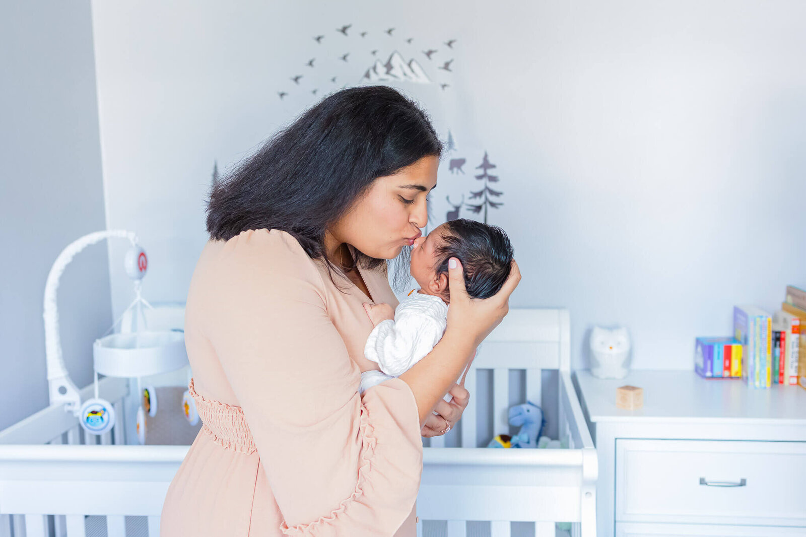 A mom kissing her newborn on the nose in the nursery.