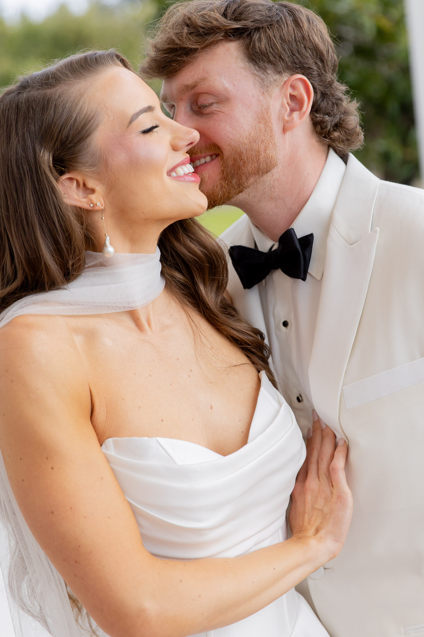A groom is about to kiss his bride on her cheek on their wedding day. The photo feels timeless and romantic.