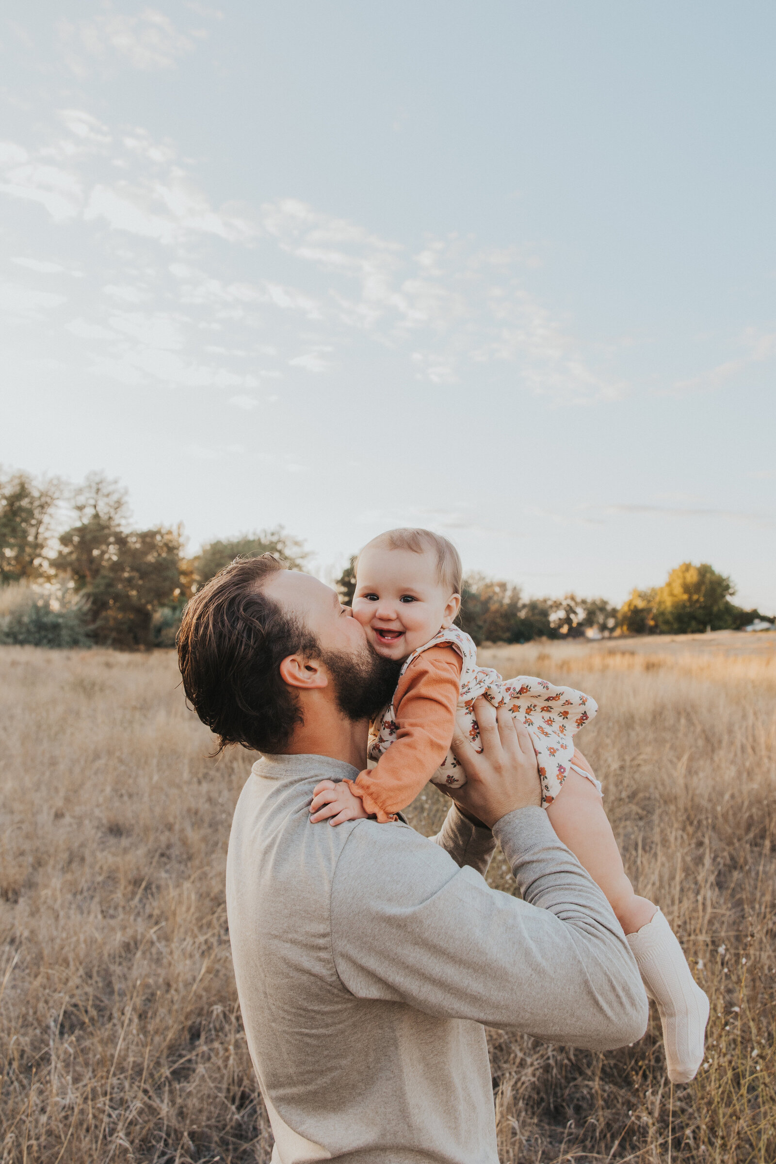 Dad stands in a field while kissing his daughters cheek