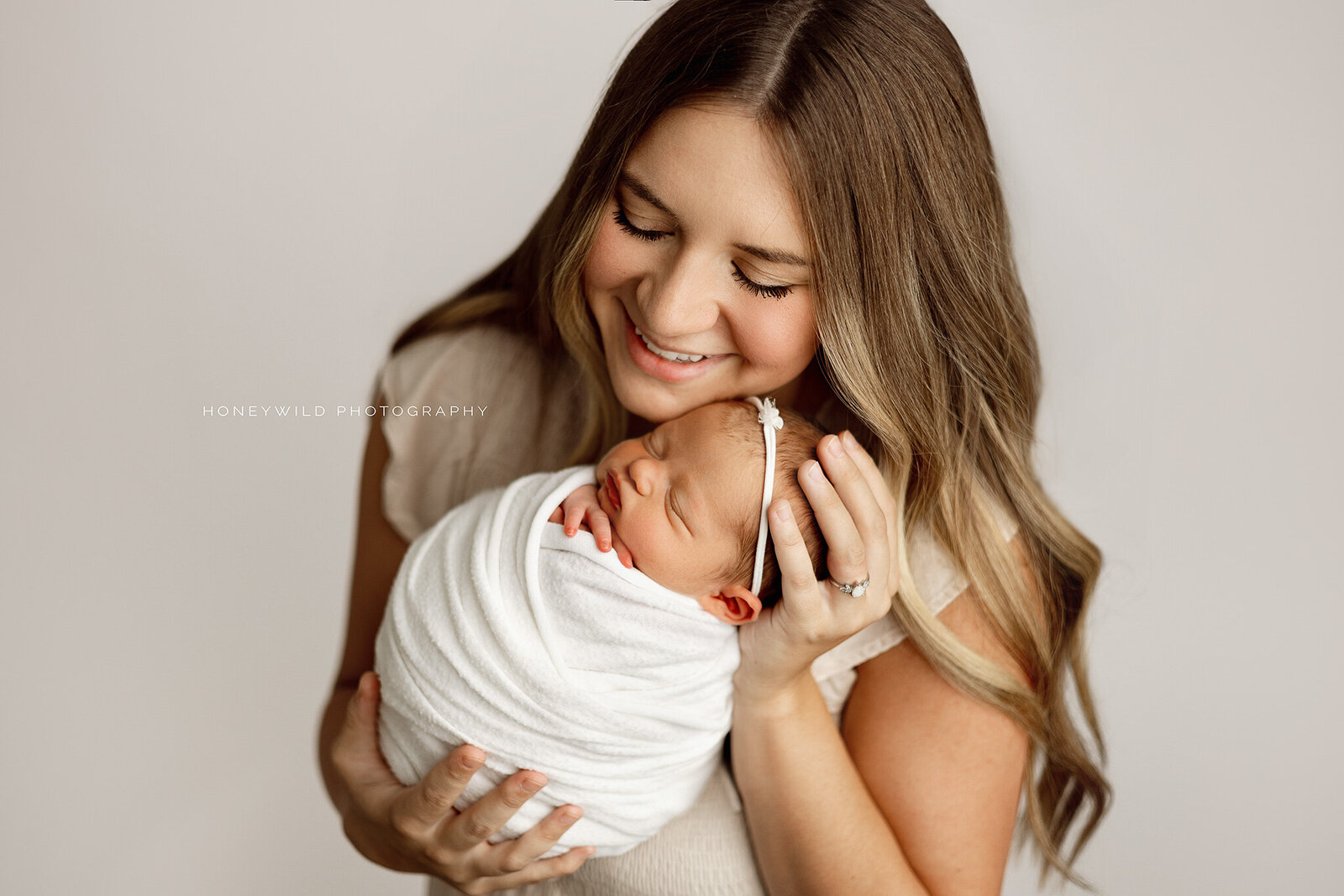 Smiling mother cradling her swaddled newborn baby during a luxury newborn session, photographed by Honeywild Photography in Grand Rapids, MI