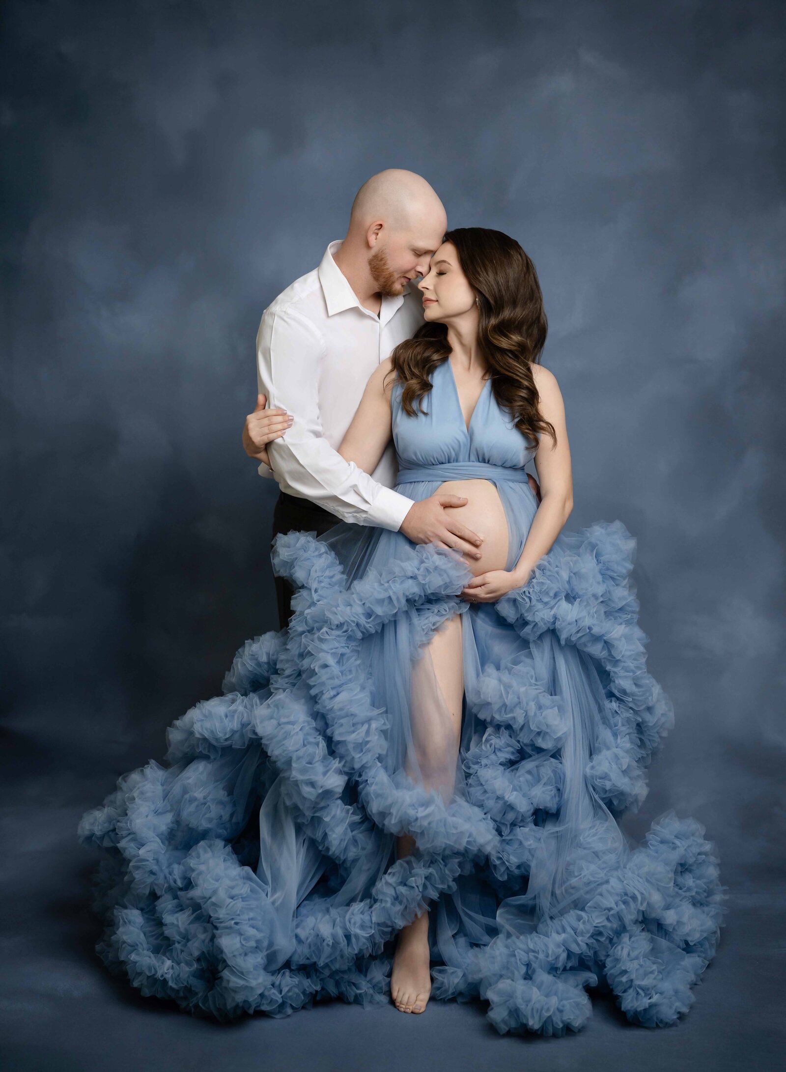 Blue watercolor backdrop with Mom in Blue ruffled maternity dress, snuggled in with dad. Maternity Photo by Jenni Nikki Photography, Atlanta maternity Photographer.