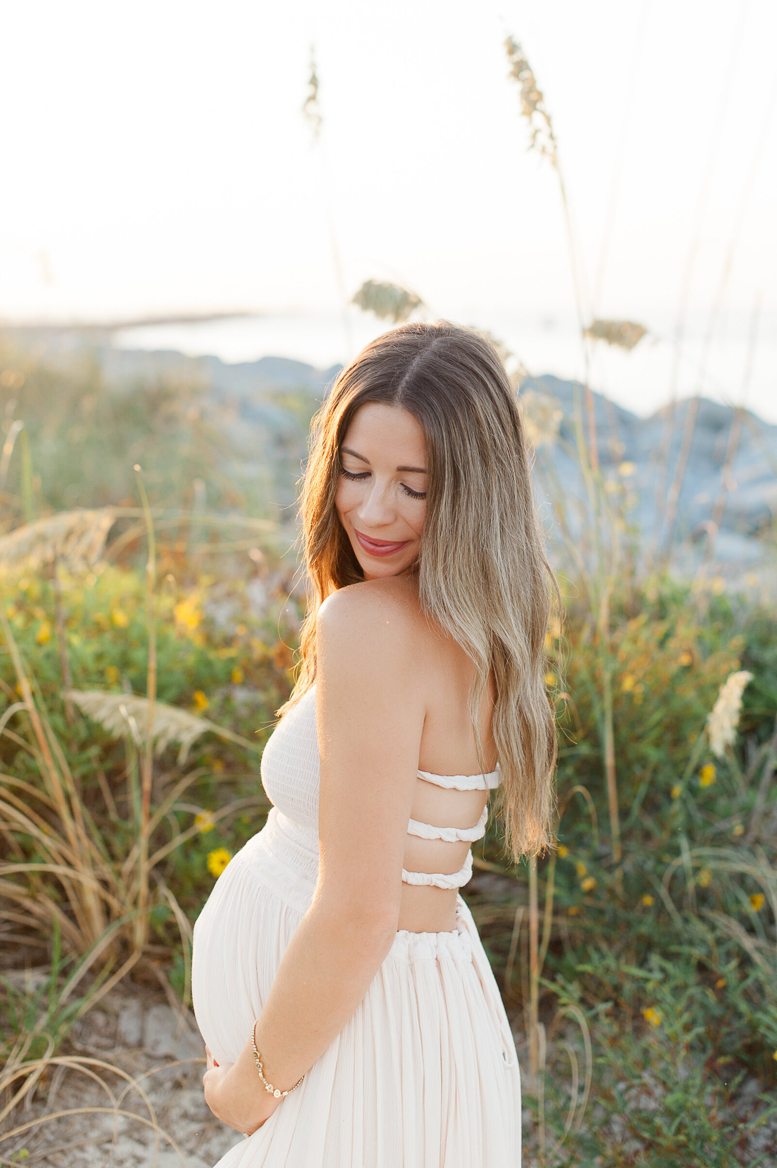 Pregnant mother standing on the beach looking down over her shoulder at sunrise