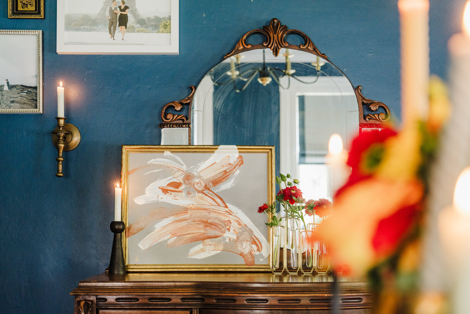 a large framed piece of art is displayed on a mirrored chest alongside candles and flowers