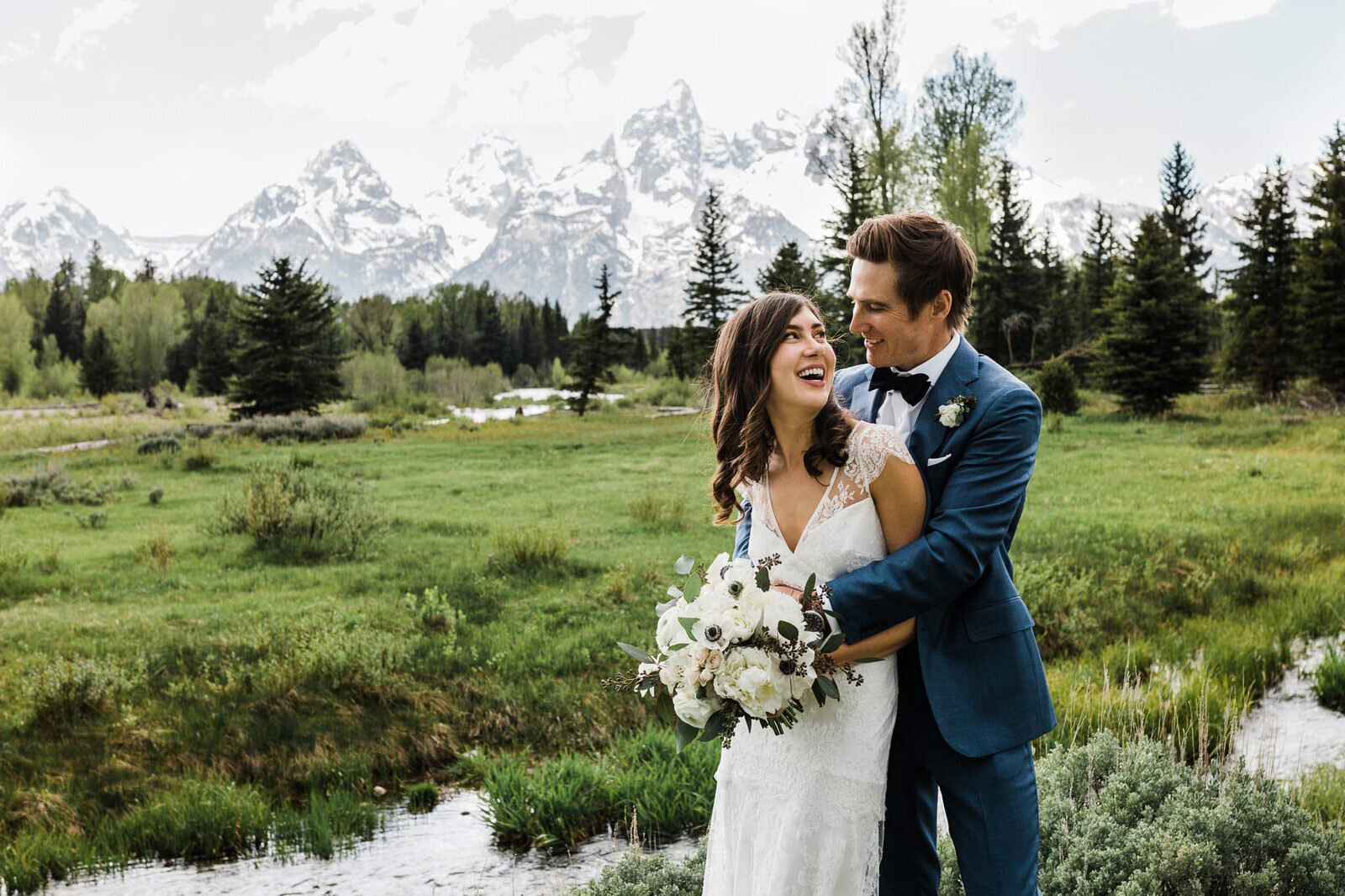 A couple laughs together near a river on their wedding day in Grand Teton National Park
