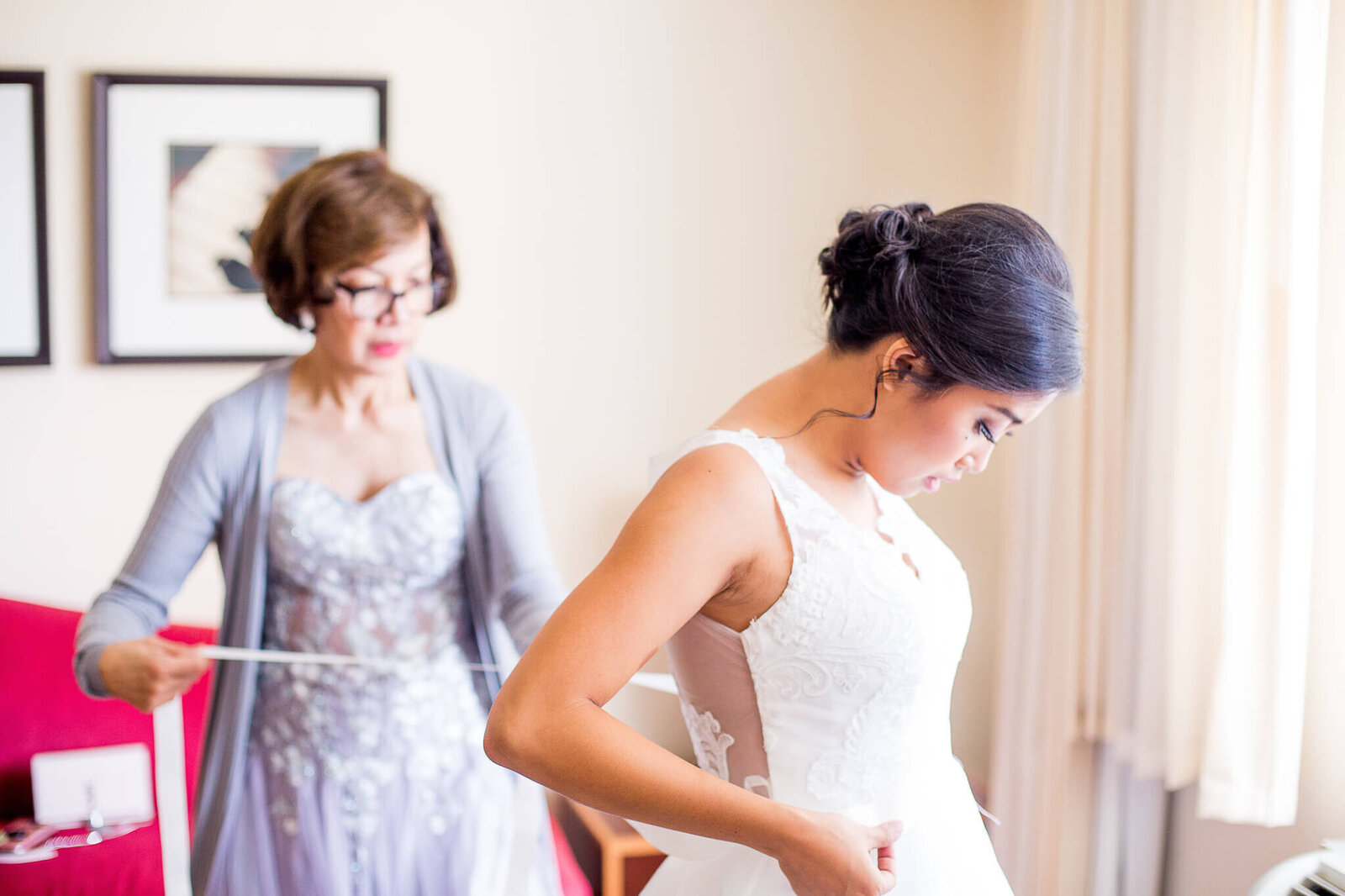 Mother of bride assisting bride with wedding dress.