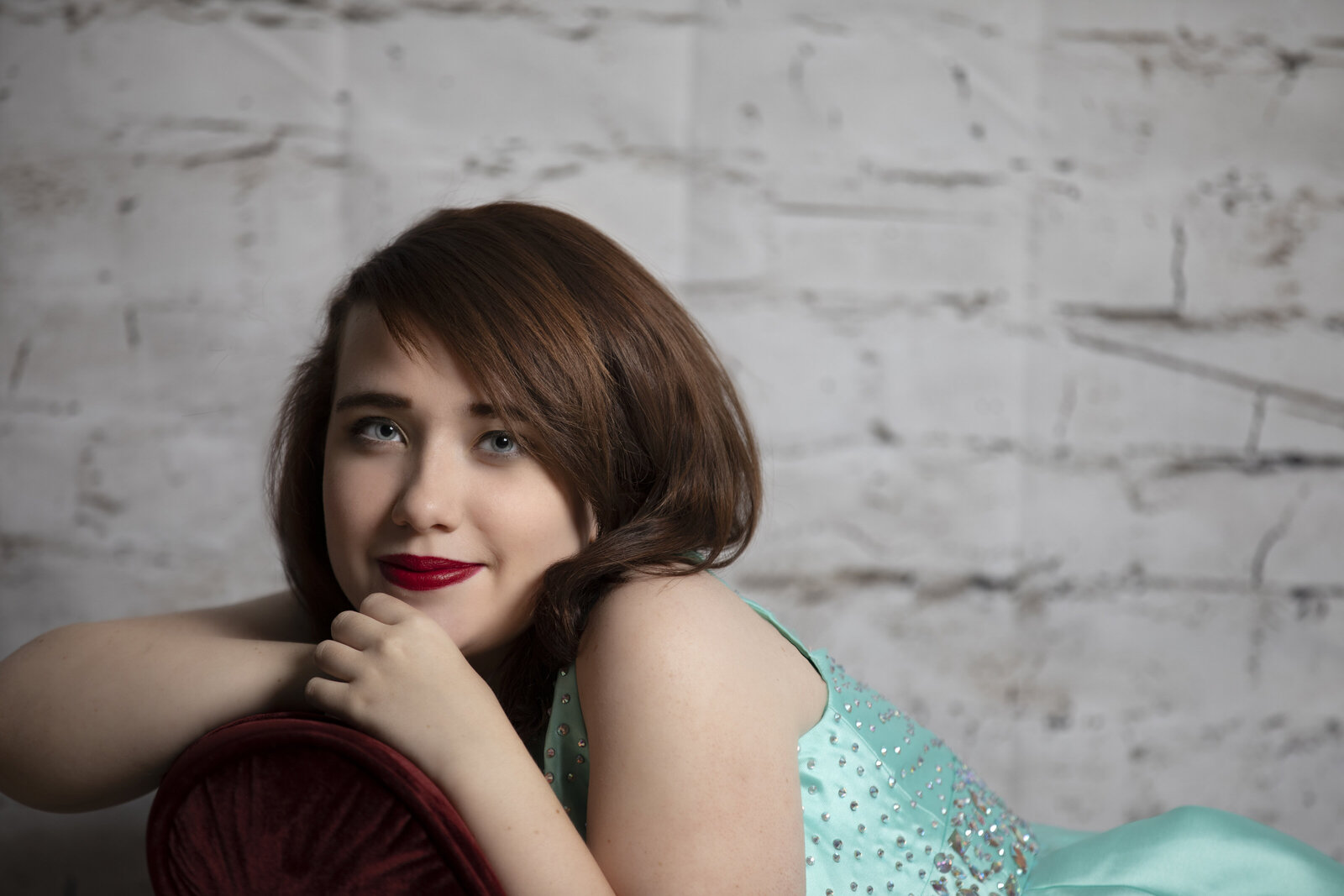 Senior poses on a red sofa during a senior photo session