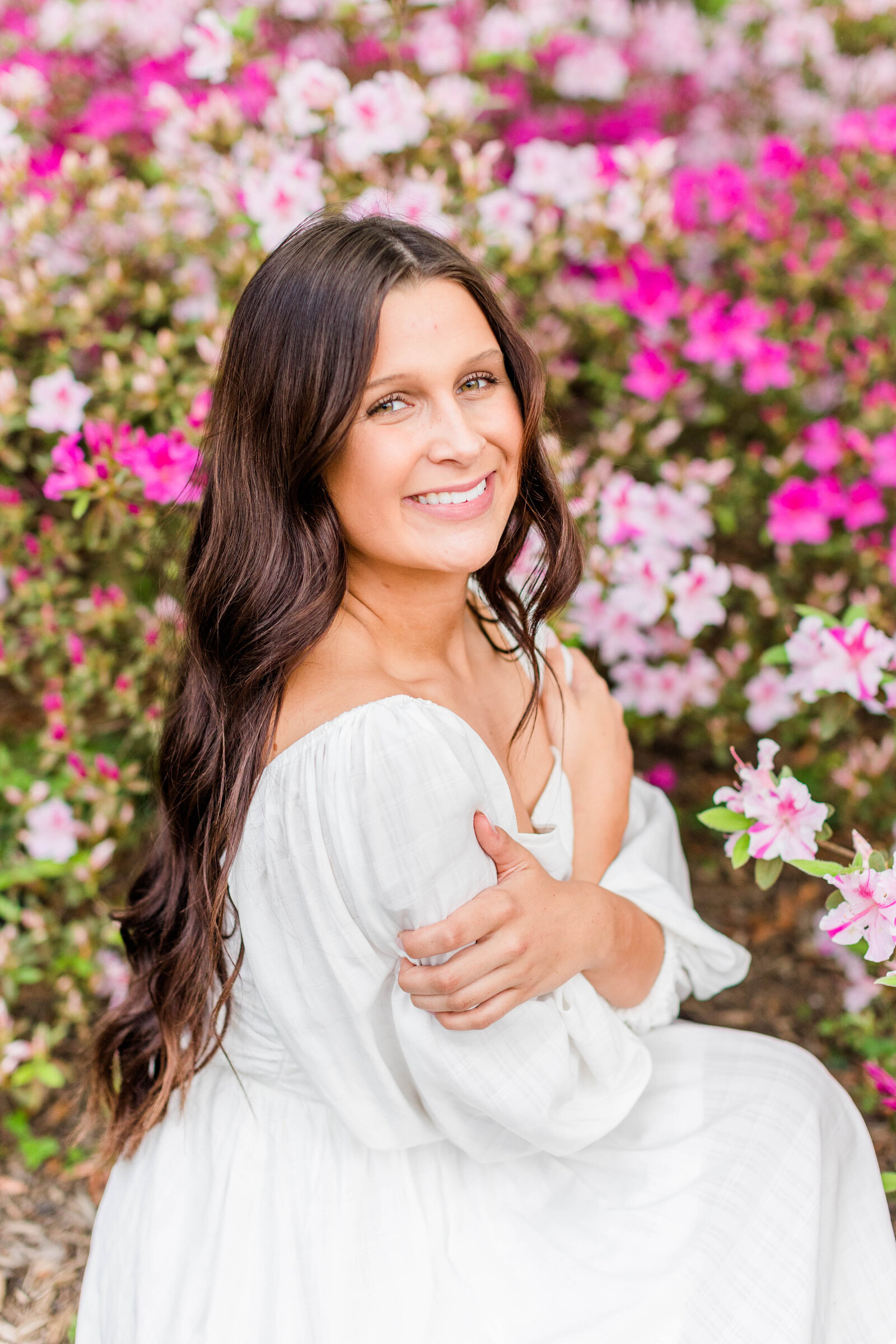 senior posing in white dress in front of pink flowers