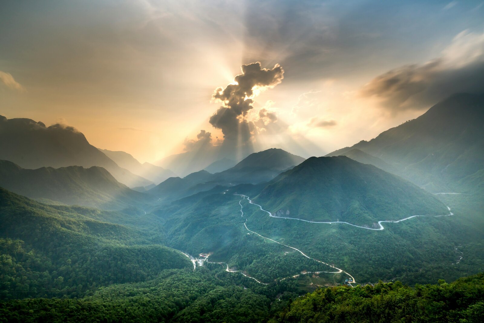 Image of a mountain range with a sun rays coming out of clouds above.